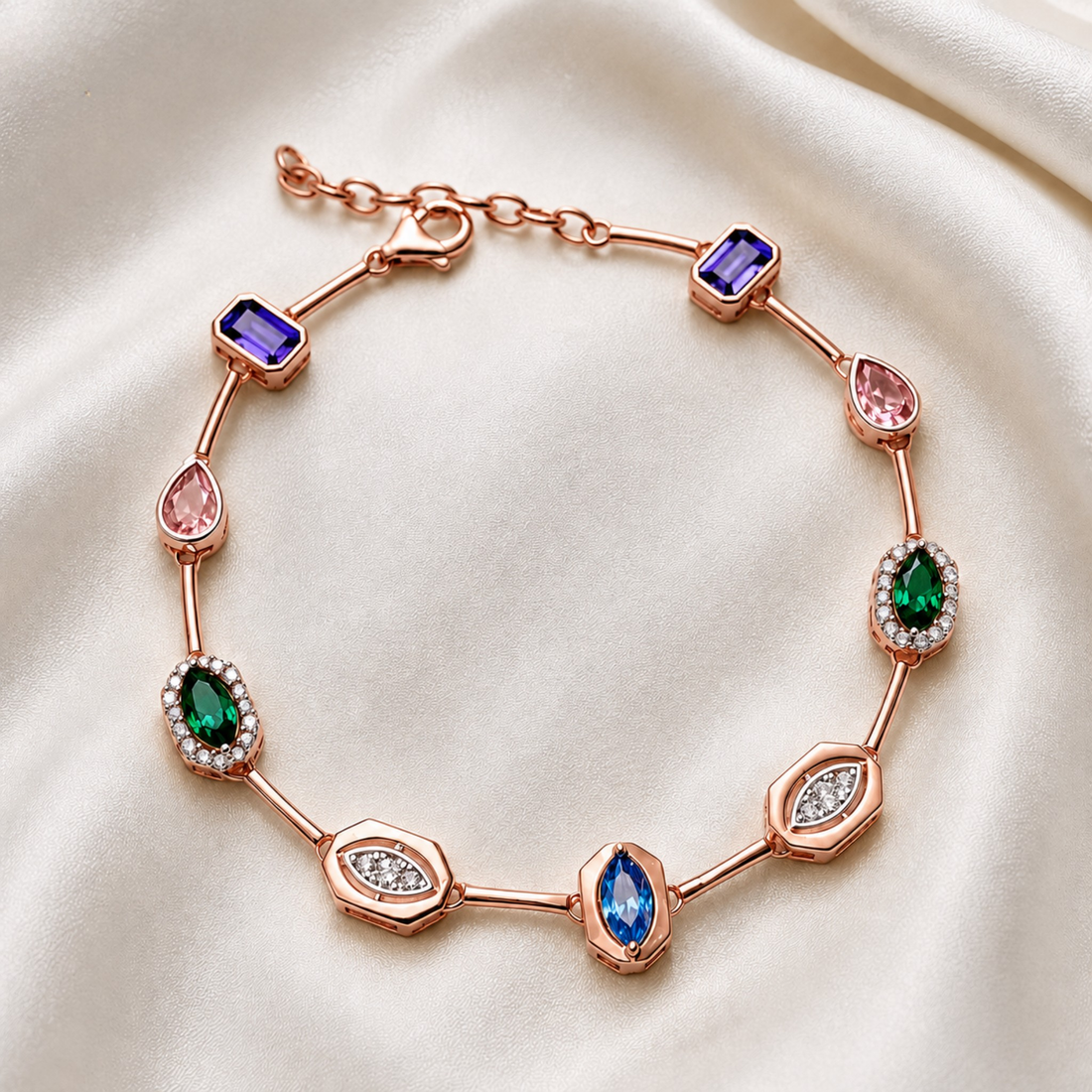 A rose gold bracelet featuring multiple colorful gemstones in various shapes, displayed on a draped cream satin fabric background.
