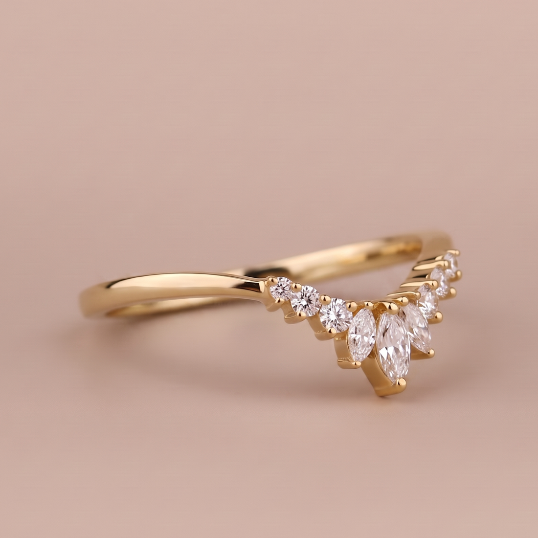 A gold ring with a marquise-cut diamond center and smaller round diamonds along the band, set against a solid warm beige background.