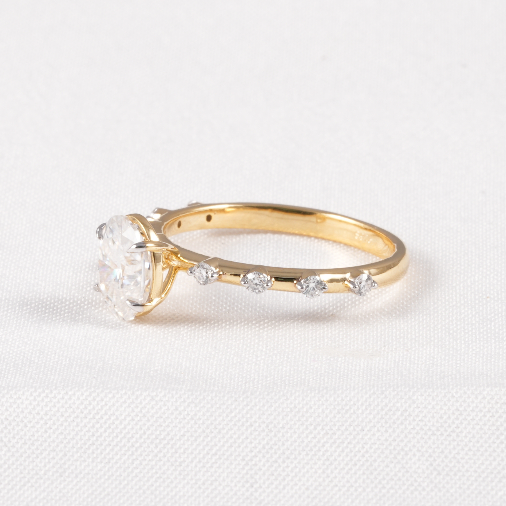 A yellow gold ring featuring a large clear heart-shaped gemstone in a prong setting, with smaller clear marquise-cut stones along the band, displayed on a textured white fabric background.