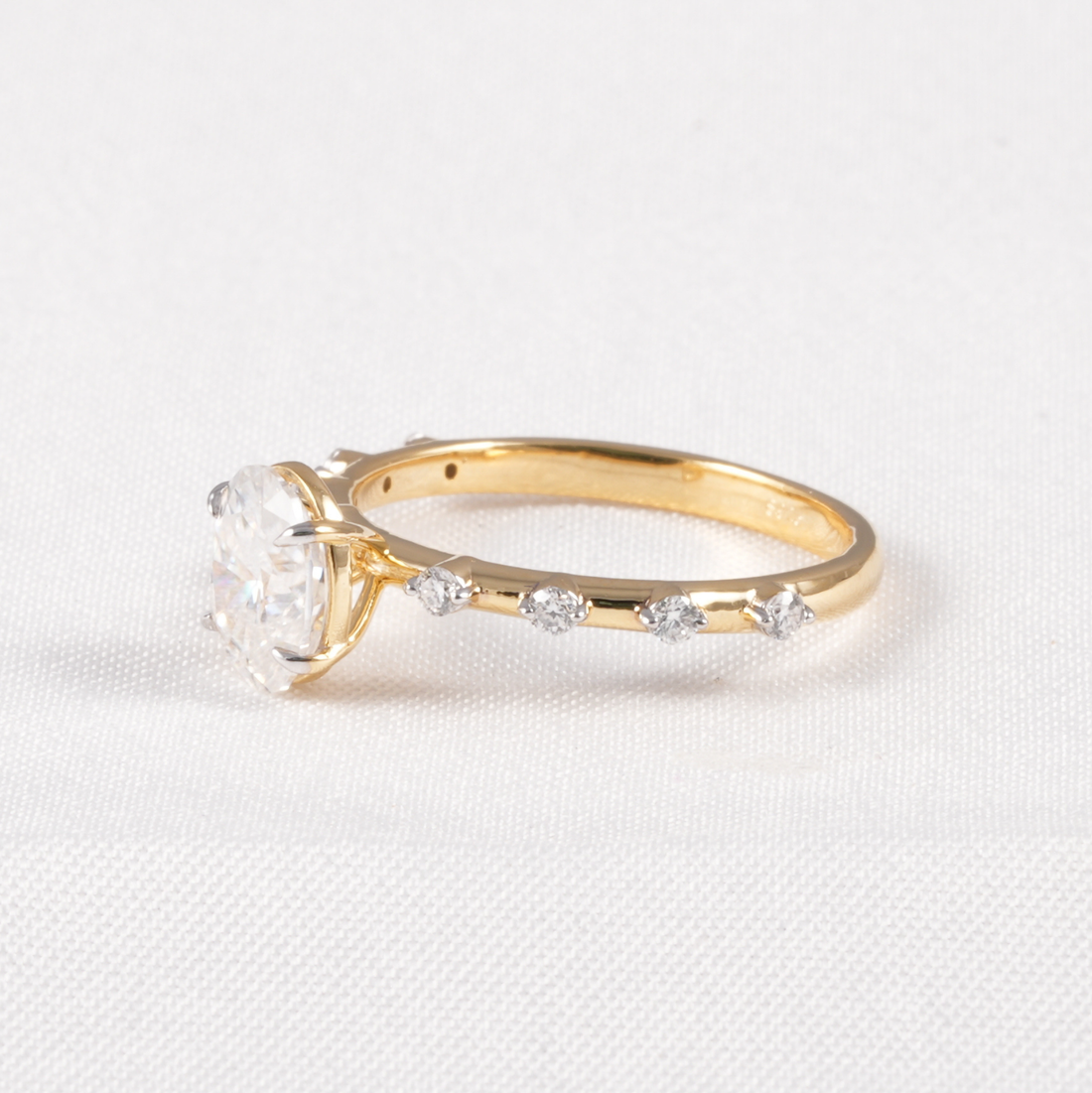 A yellow gold ring featuring a large clear heart-shaped gemstone in a prong setting, with smaller clear marquise-cut stones along the band, displayed on a textured white fabric background.