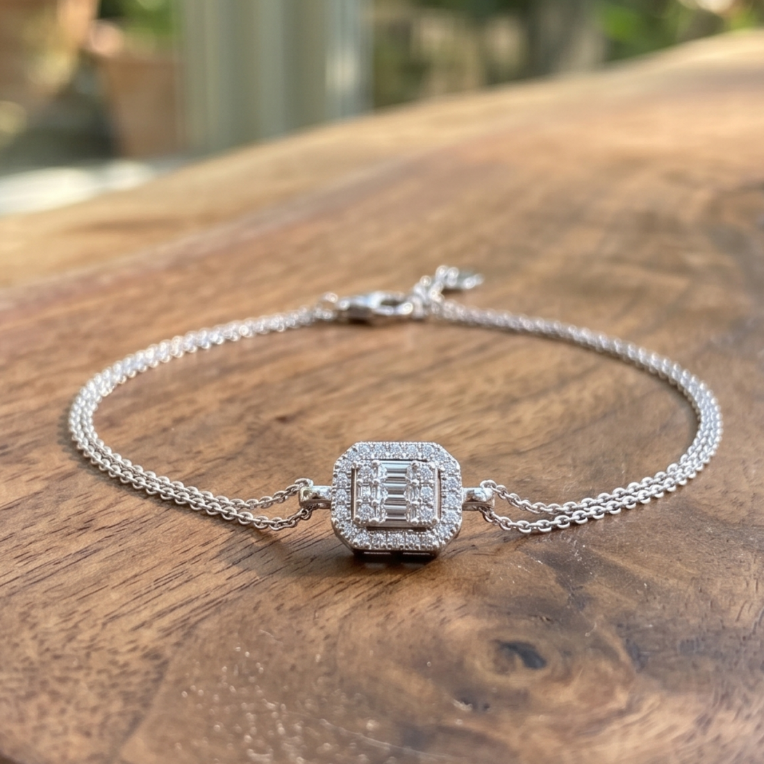 A silver-toned chain bracelet with a square pavé charm featuring a central emerald-cut style diamond, resting on a rustic wooden surface.