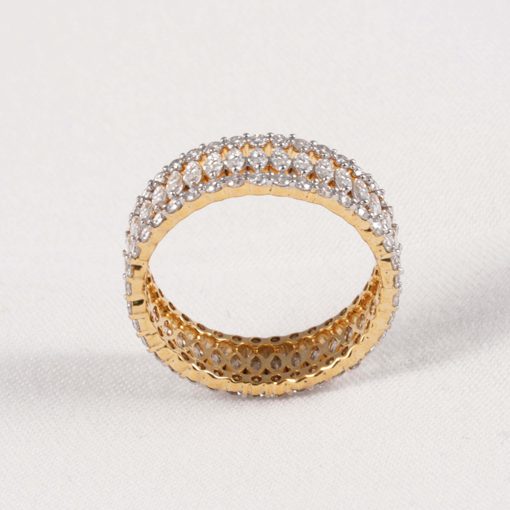 A yellow gold ring with a double row of clear pavé gemstones on the outer band and a textured openwork inner band, shown on a light gray background.