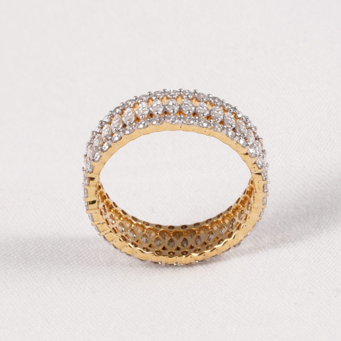 A yellow gold ring with a double row of clear pavé gemstones on the outer band and a textured openwork inner band, shown on a light gray background.