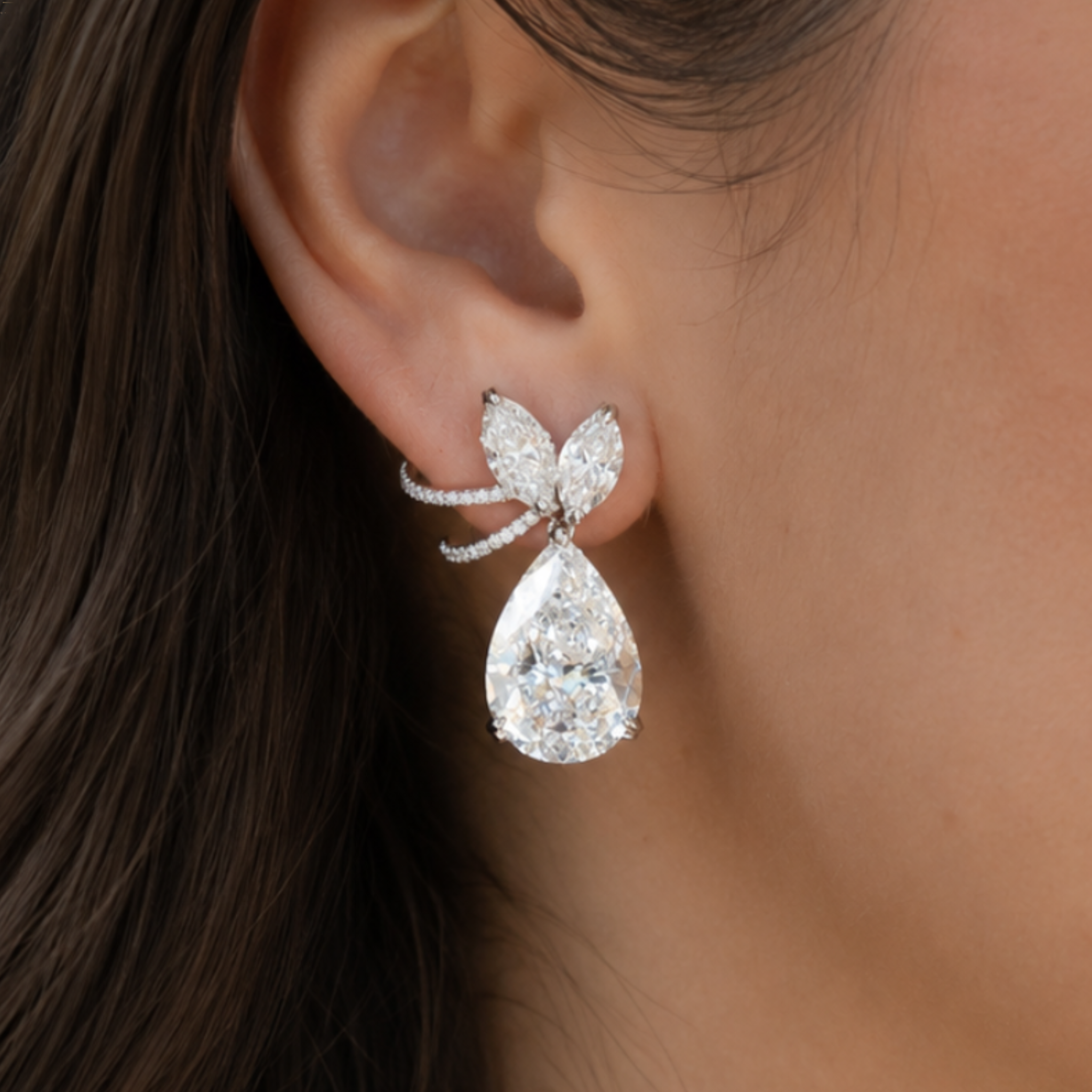 A close-up of a model's ear wearing a silver butterfly earring with a large pear-cut clear gemstone and smaller round stones.