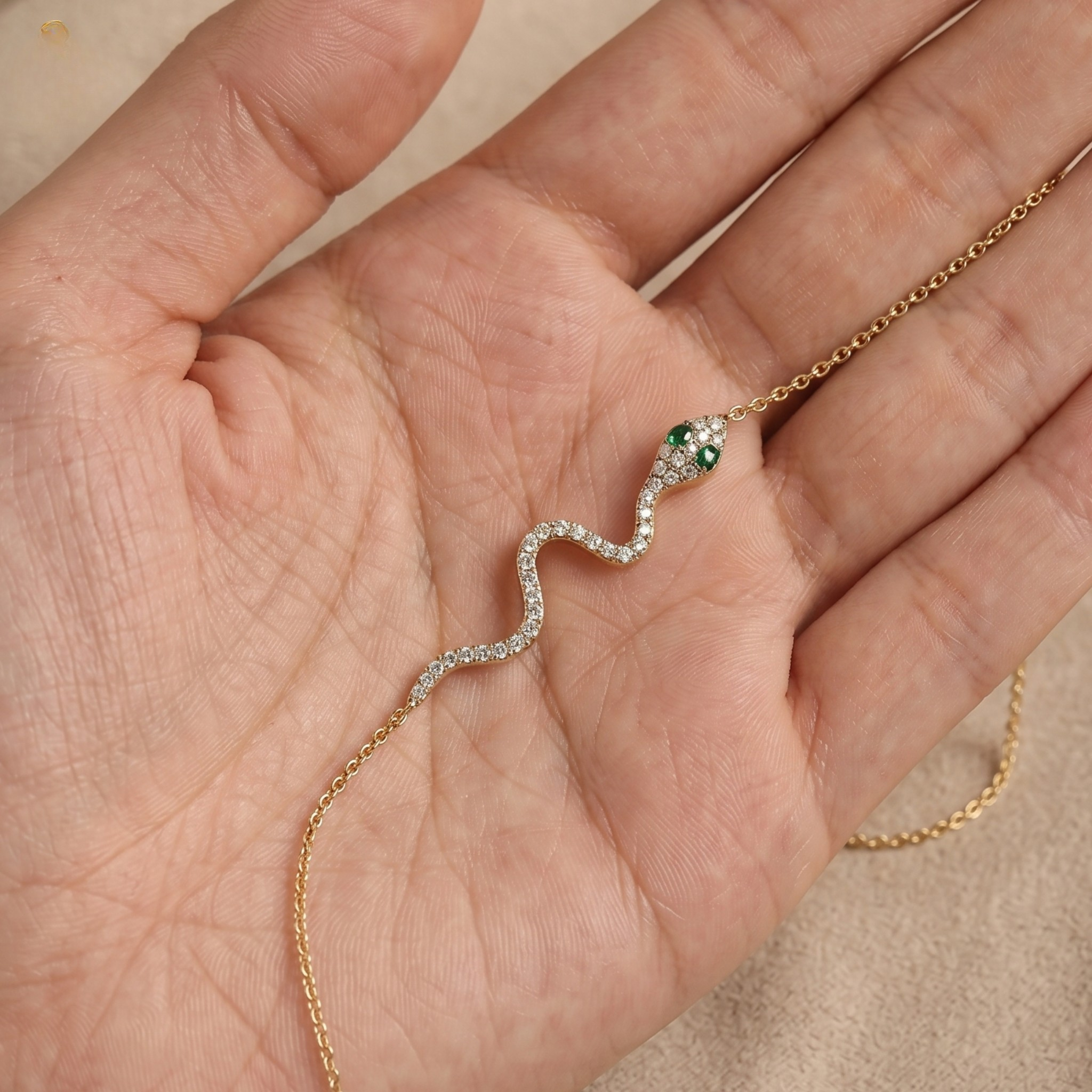 A delicate snake-shaped necklace with a green head and clear stones along its body, resting on an open hand.
