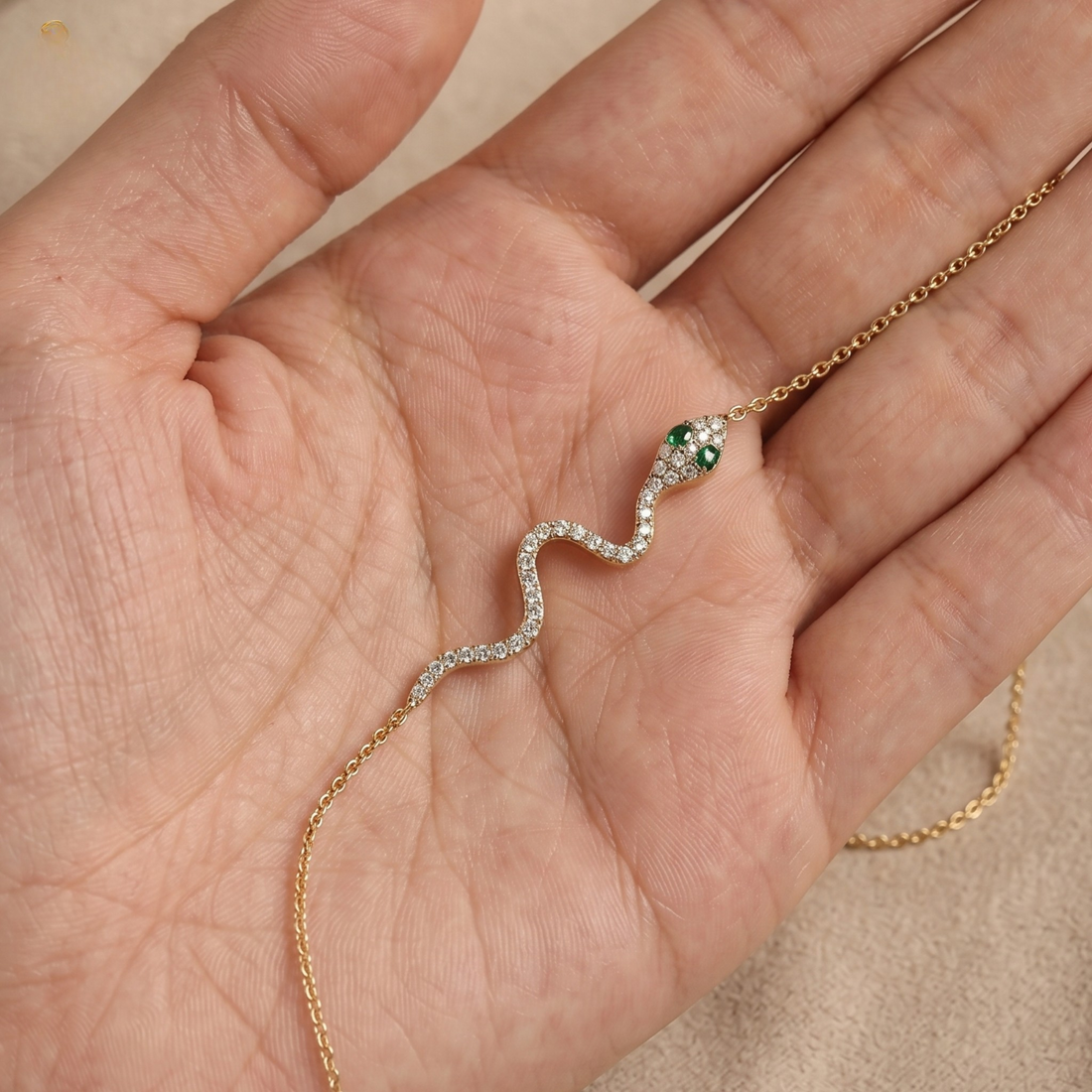 A delicate snake-shaped necklace with a green head and clear stones along its body, resting on an open hand.