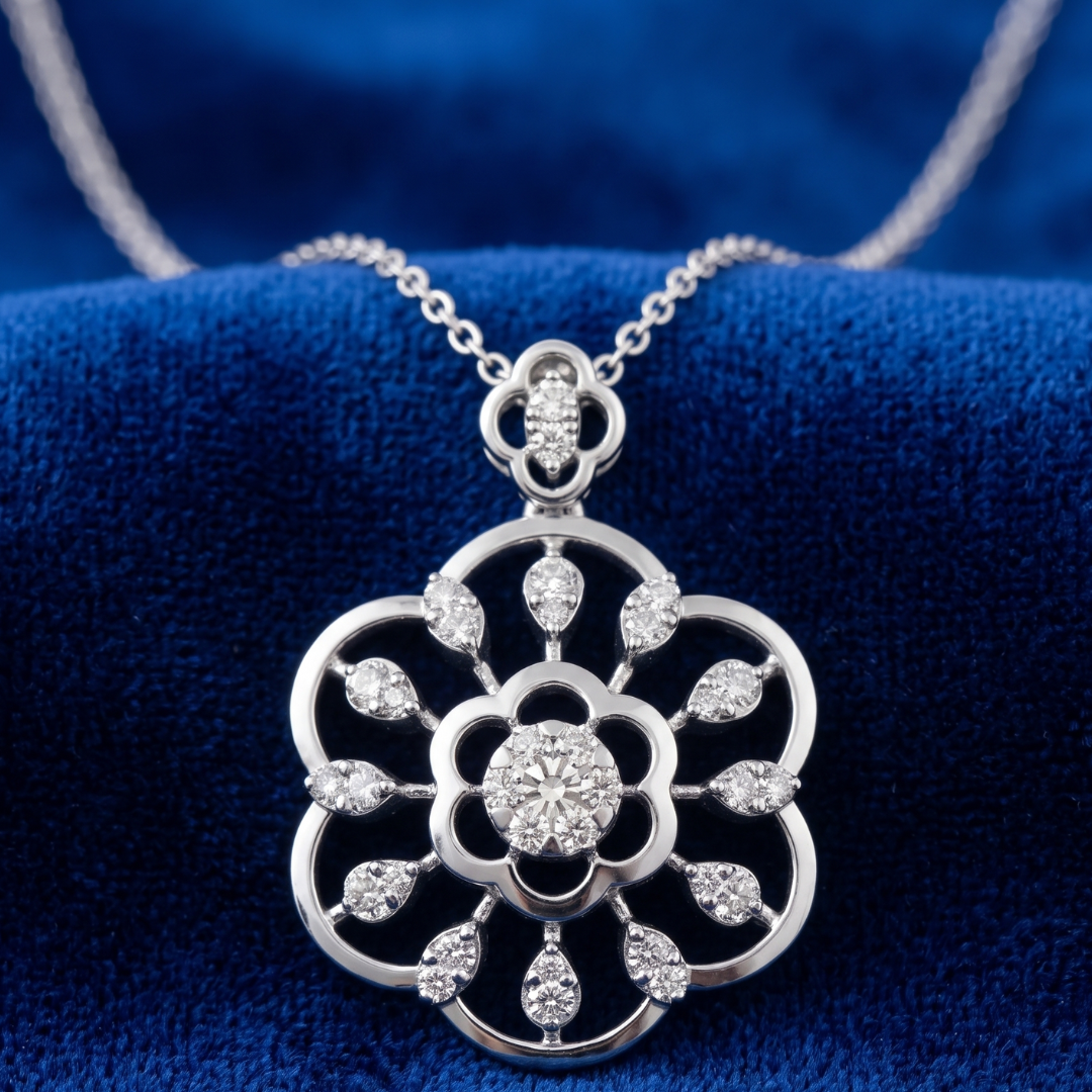 A silver-tone floral pendant necklace with clear round and teardrop-cut gemstones, displayed on a deep blue velvet surface.