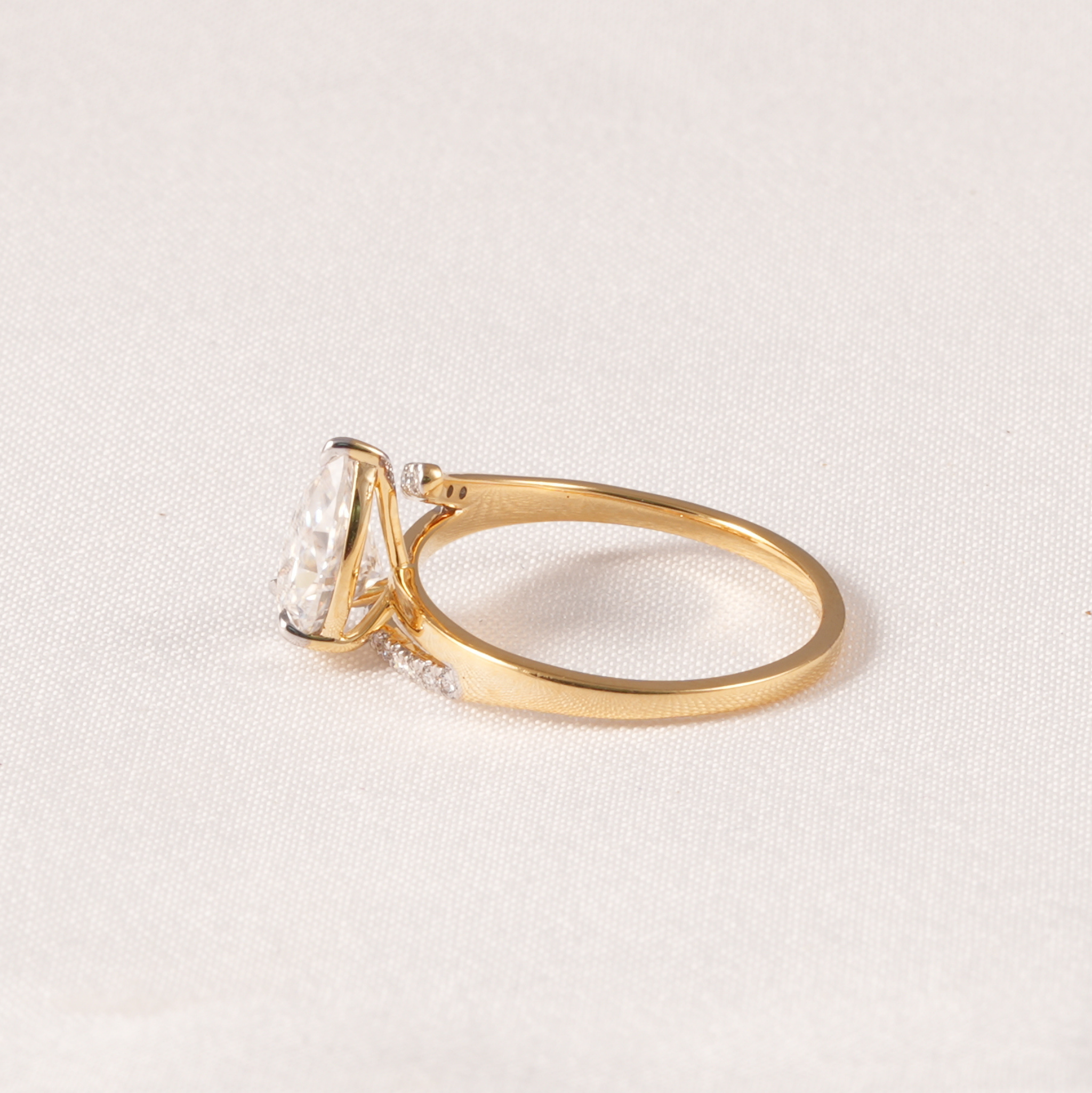 A yellow gold ring featuring a large rectangular clear gemstone in a prong setting, with small accent stones along the band, photographed on a light textured fabric background.