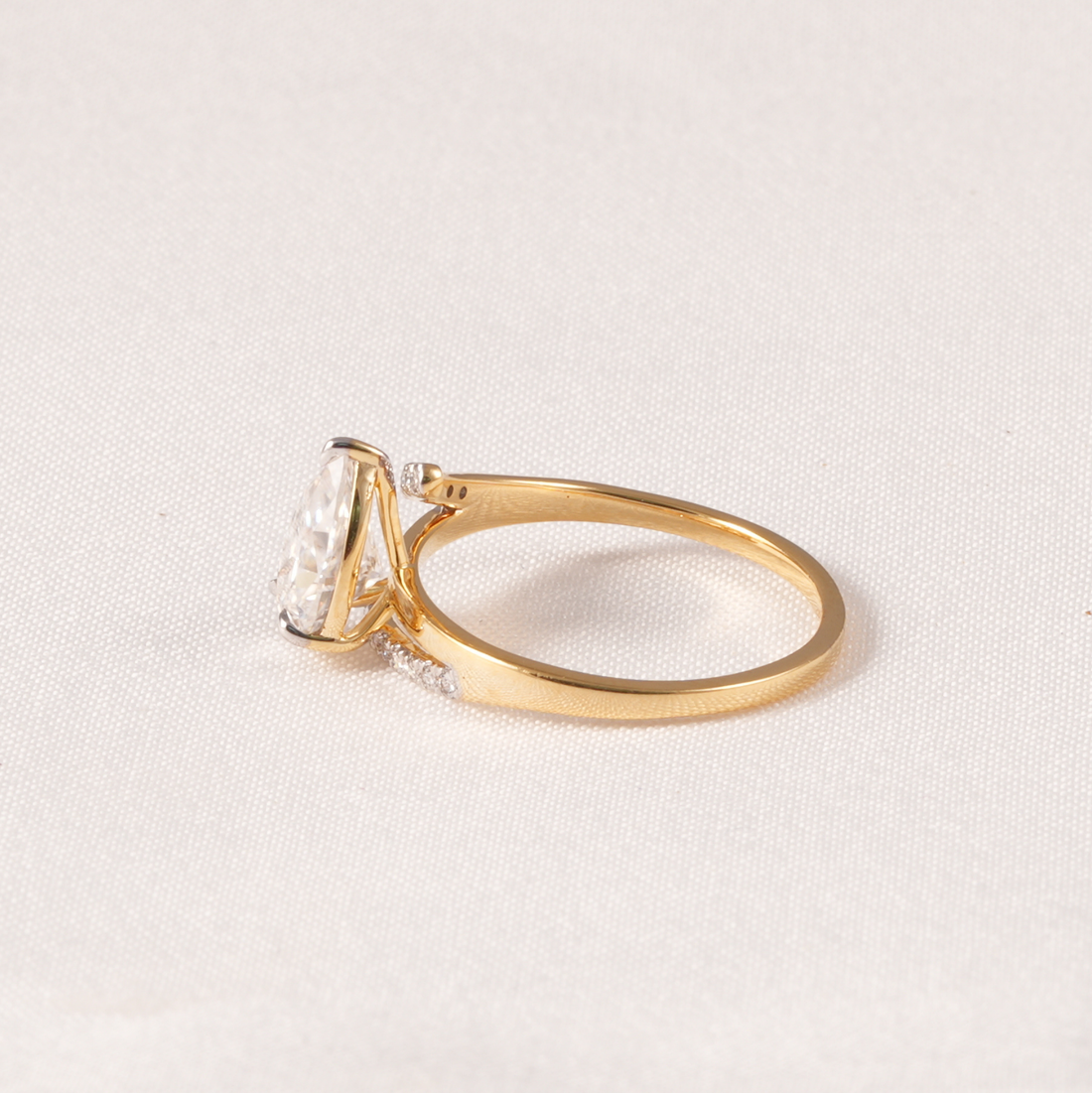 A yellow gold ring featuring a large rectangular clear gemstone in a prong setting, with small accent stones along the band, photographed on a light textured fabric background.
