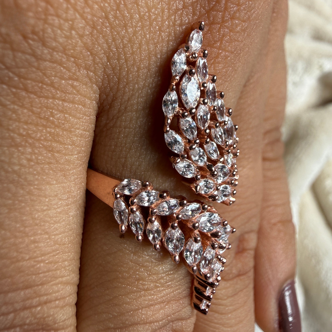 Rose gold wrap ring with marquise and oval clear gemstones, shown worn on a finger.