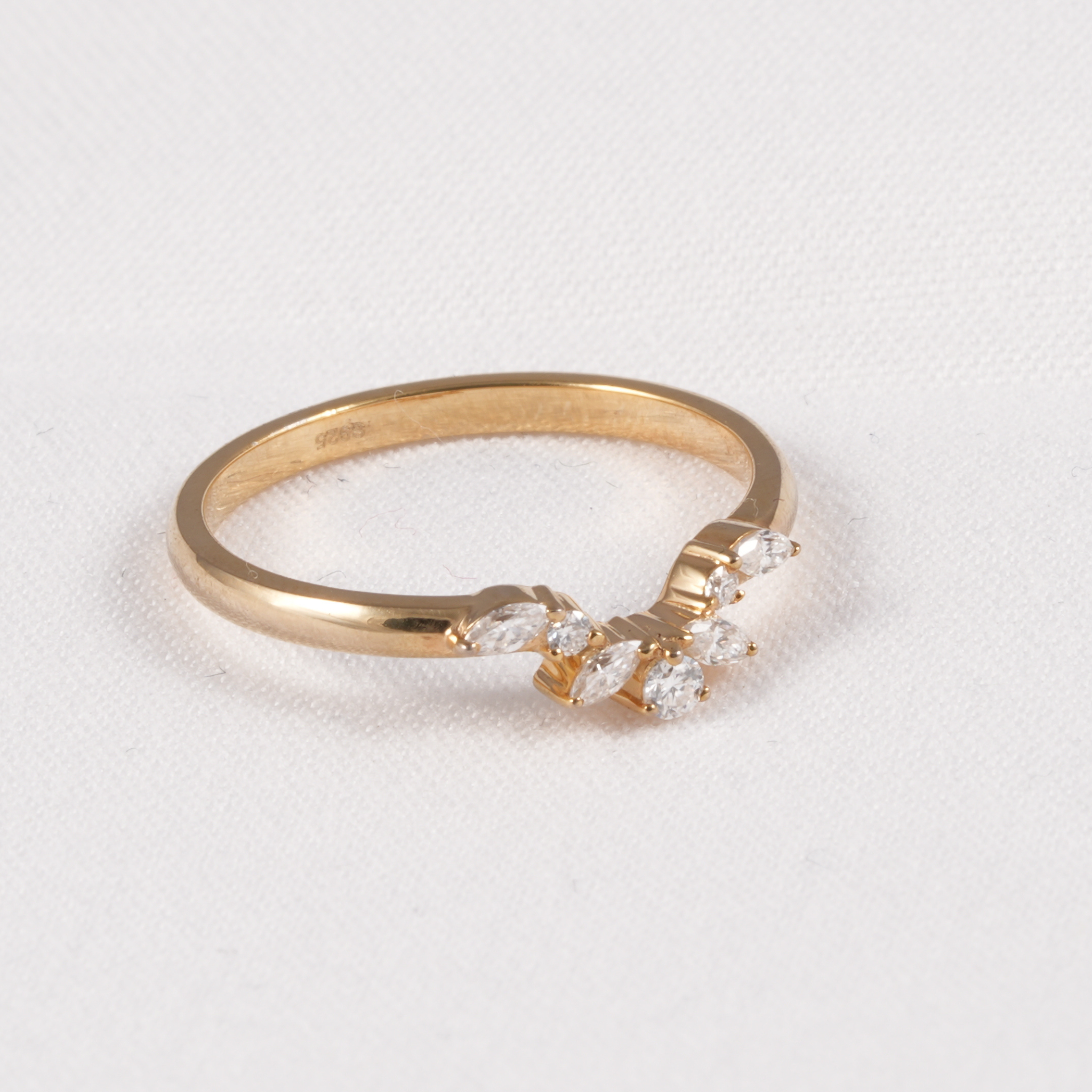 A yellow gold ring featuring a marquise-cut diamond cluster on the front, photographed on a textured white background.