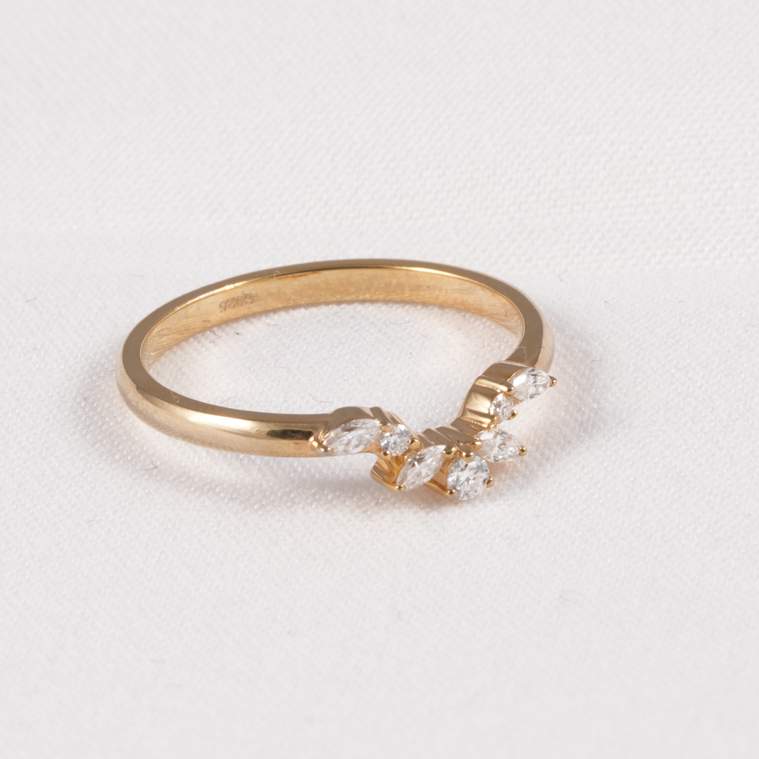 A yellow gold ring featuring a marquise-cut diamond cluster on the front, photographed on a textured white background.