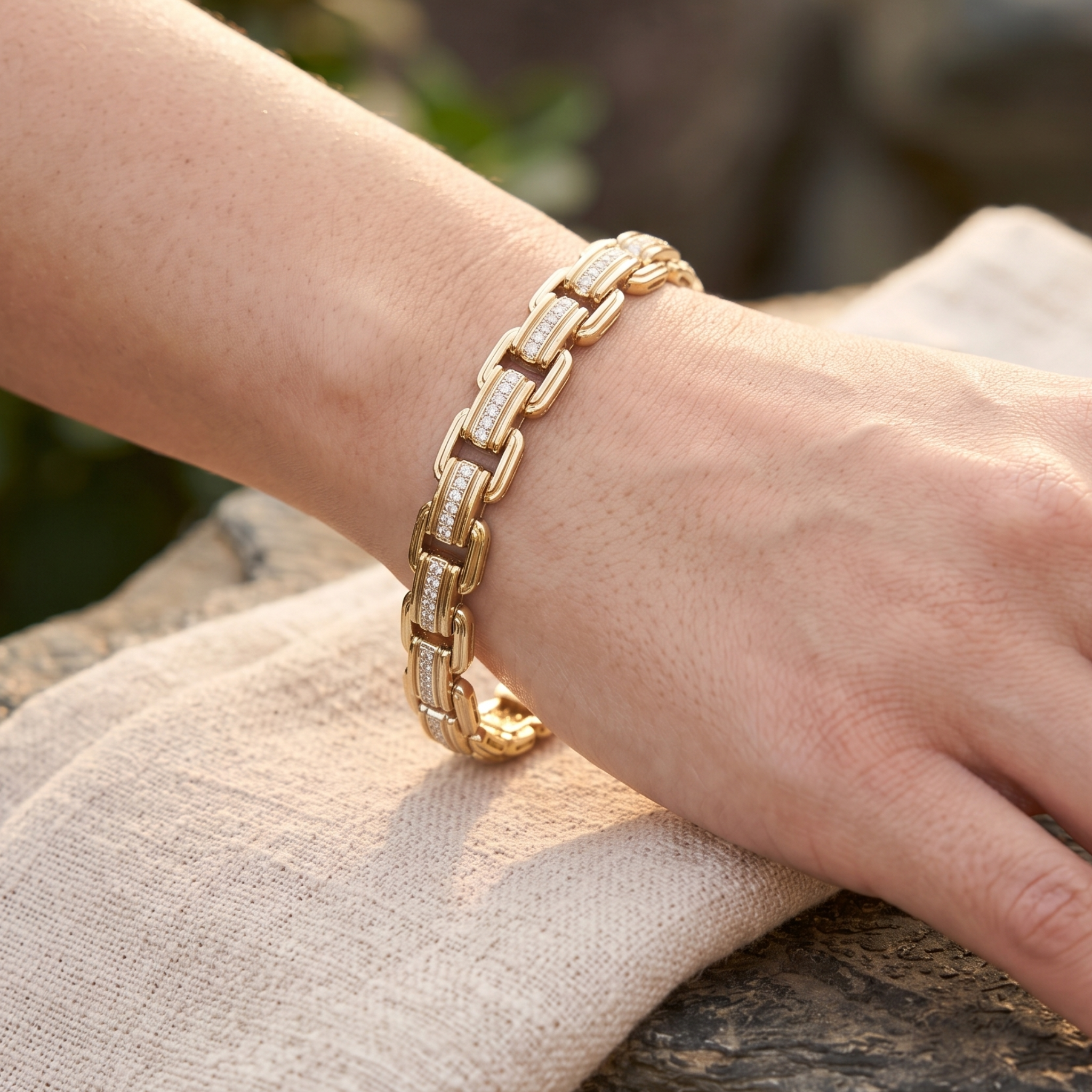 A gold link bracelet with pavé-set clear stones worn on a person's wrist, resting on a light beige linen cloth outdoors.