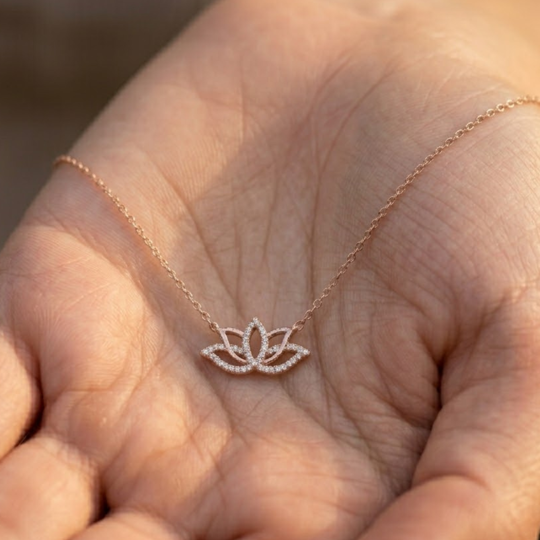 A delicate rose gold necklace with a small lotus flower pendant, resting on the palm of a hand.