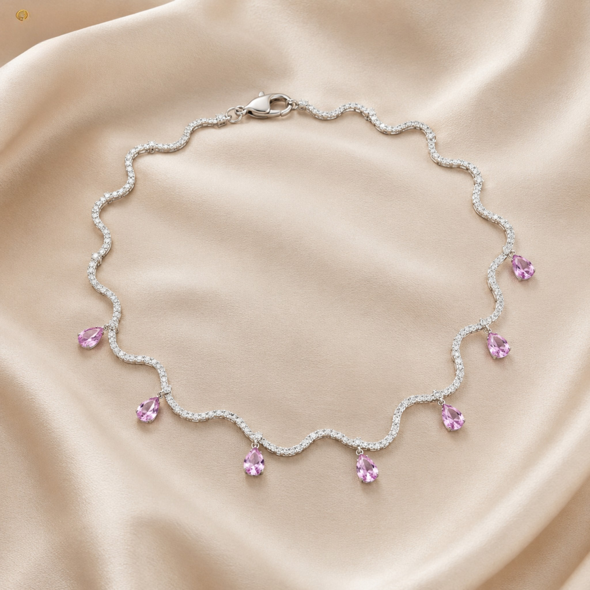 A silver-toned wavy necklace with small clear stones and dangling light pink teardrop gemstones, arranged on a soft beige satin fabric background.