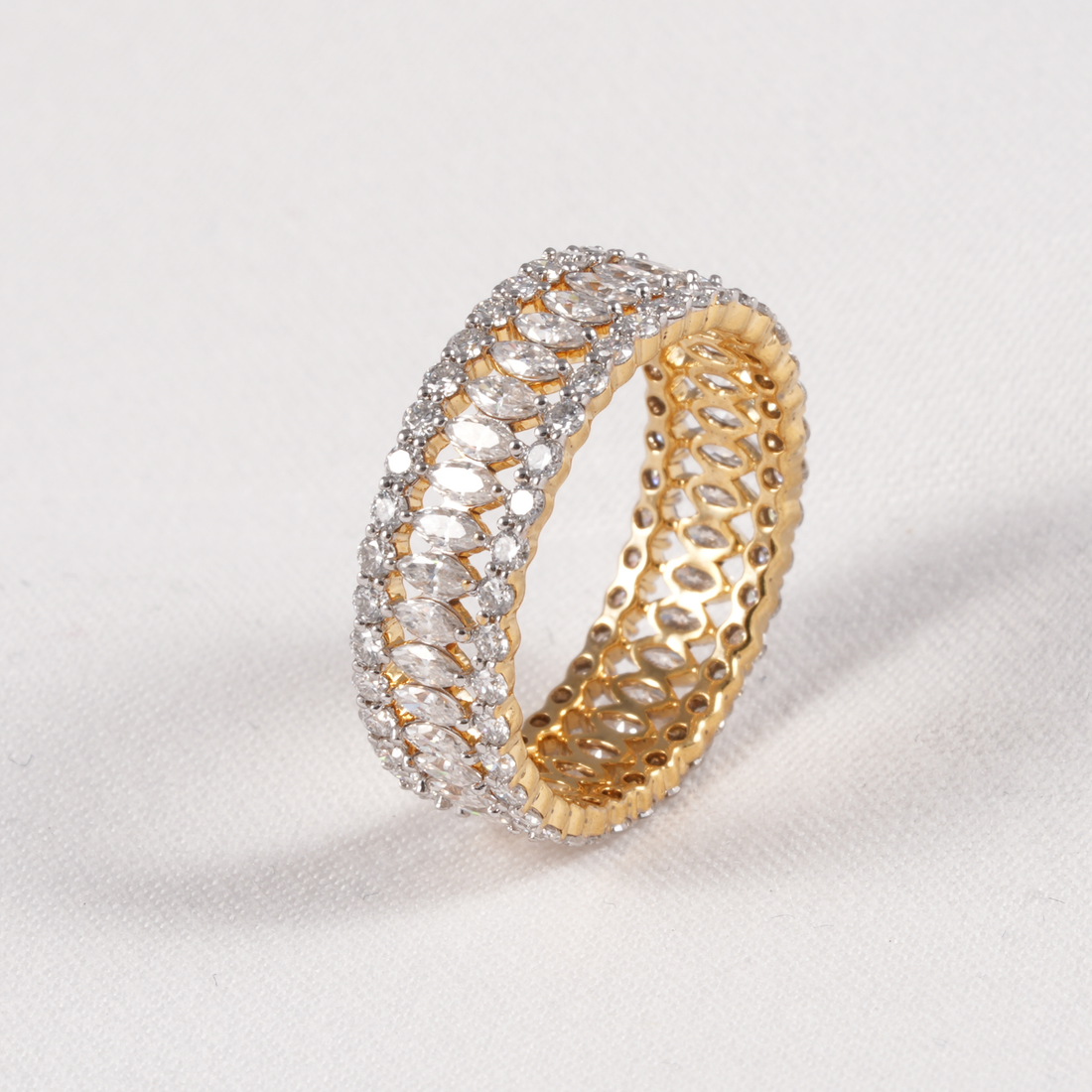 A gold eternity-style ring with rows of clear marquise-cut stones, photographed on a light neutral background.