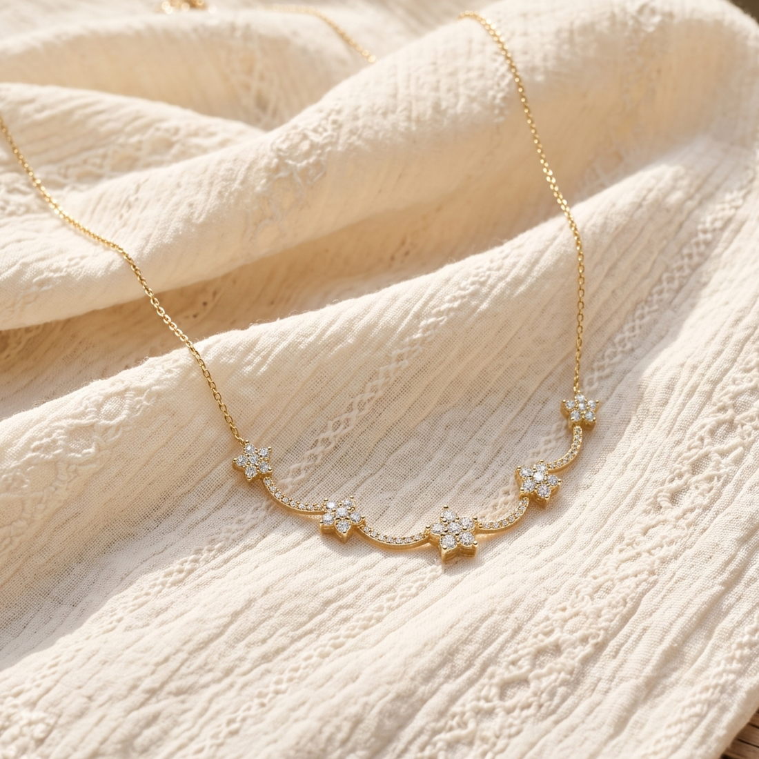 A delicate gold necklace with five small star-shaped clusters of clear stones, displayed on a textured cream-colored fabric.