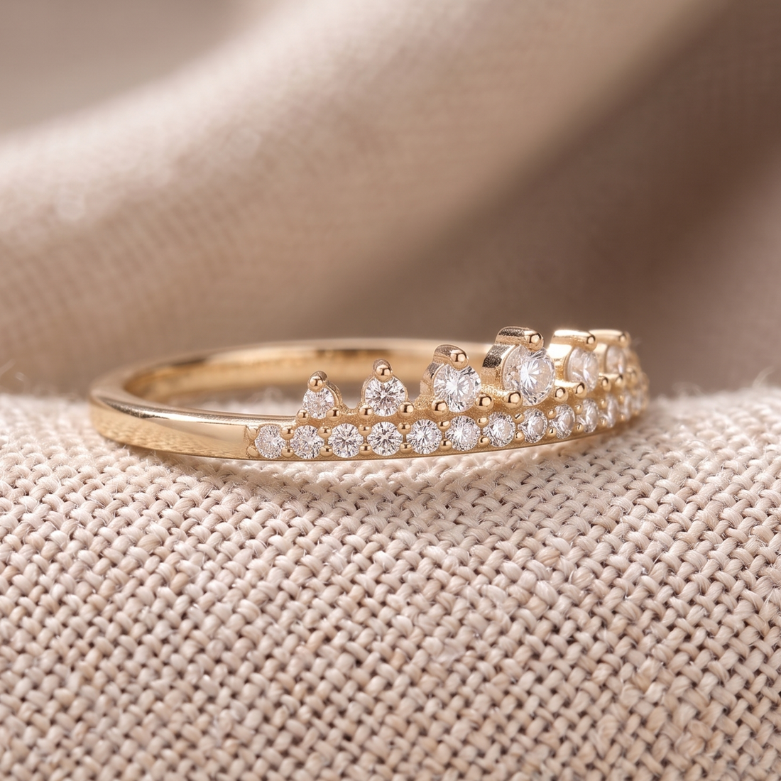 A gold ring with a row of clear gemstones, photographed close-up on a textured beige fabric background.