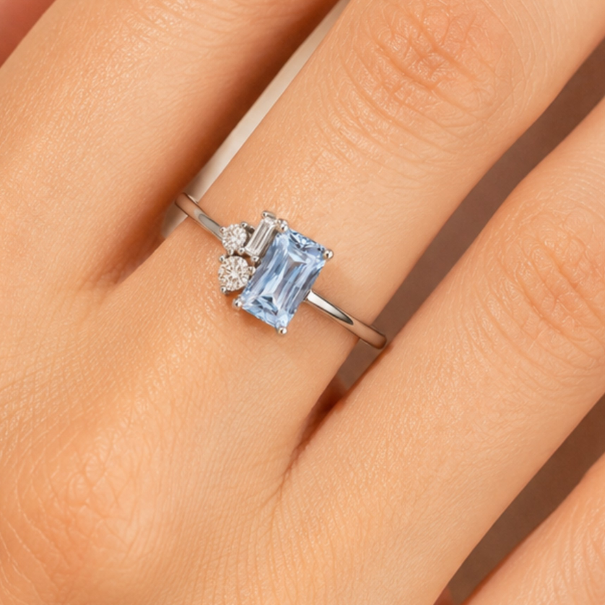 A silver ring with a rectangular light blue gemstone and small clear accent stones, shown worn on a person's finger.