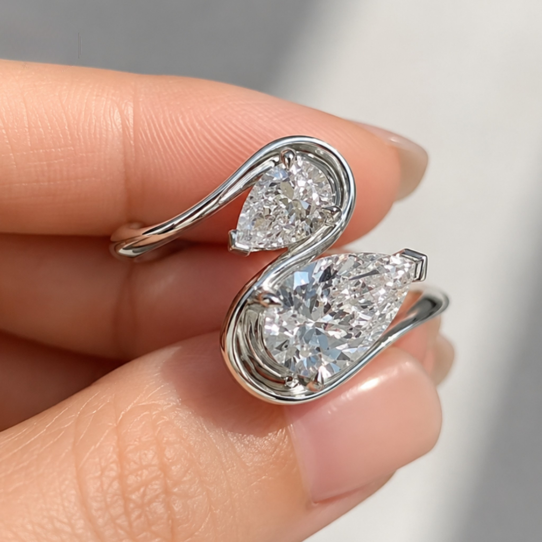 A close-up of a hand holding a silver-toned ring with two teardrop-shaped clear gemstones in a swan-like curved setting.