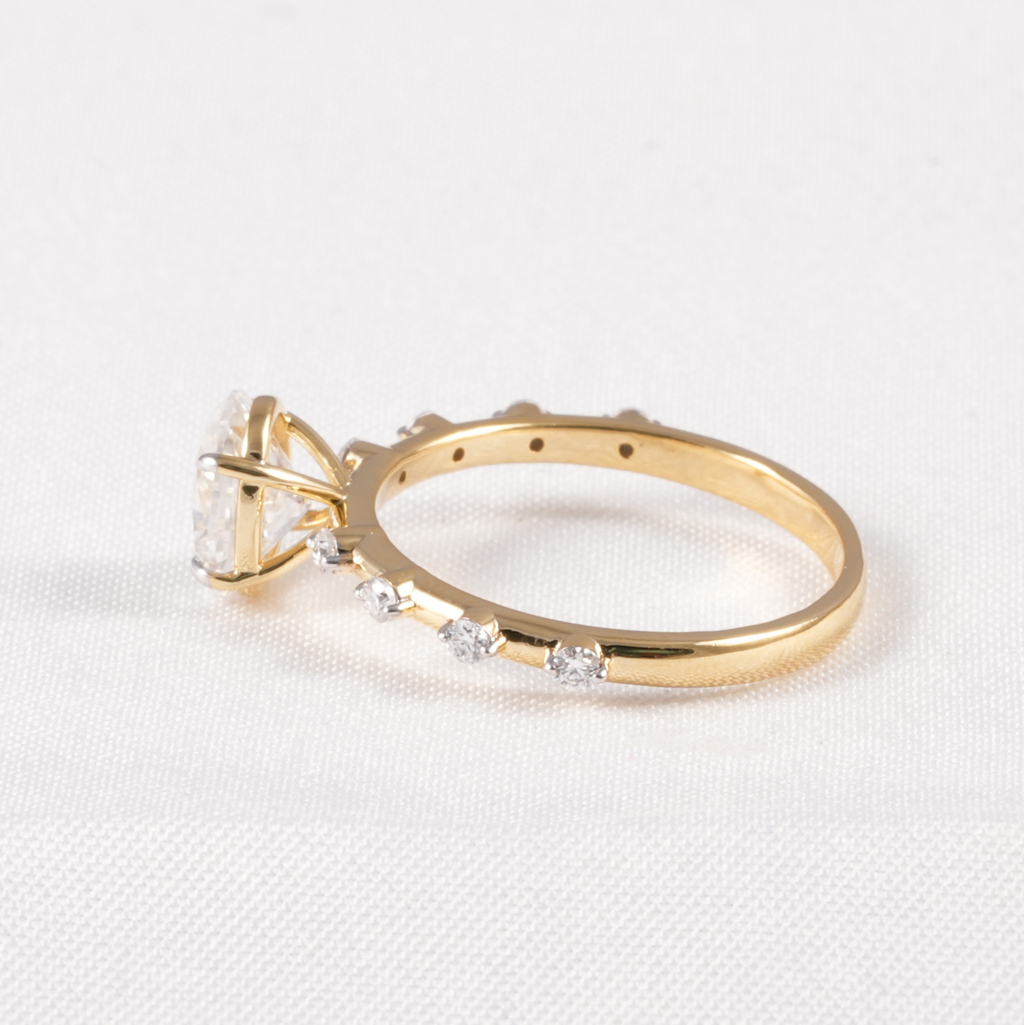 A yellow gold ring with a large clear gemstone and smaller clear stones along the band, photographed on a white textured fabric background.