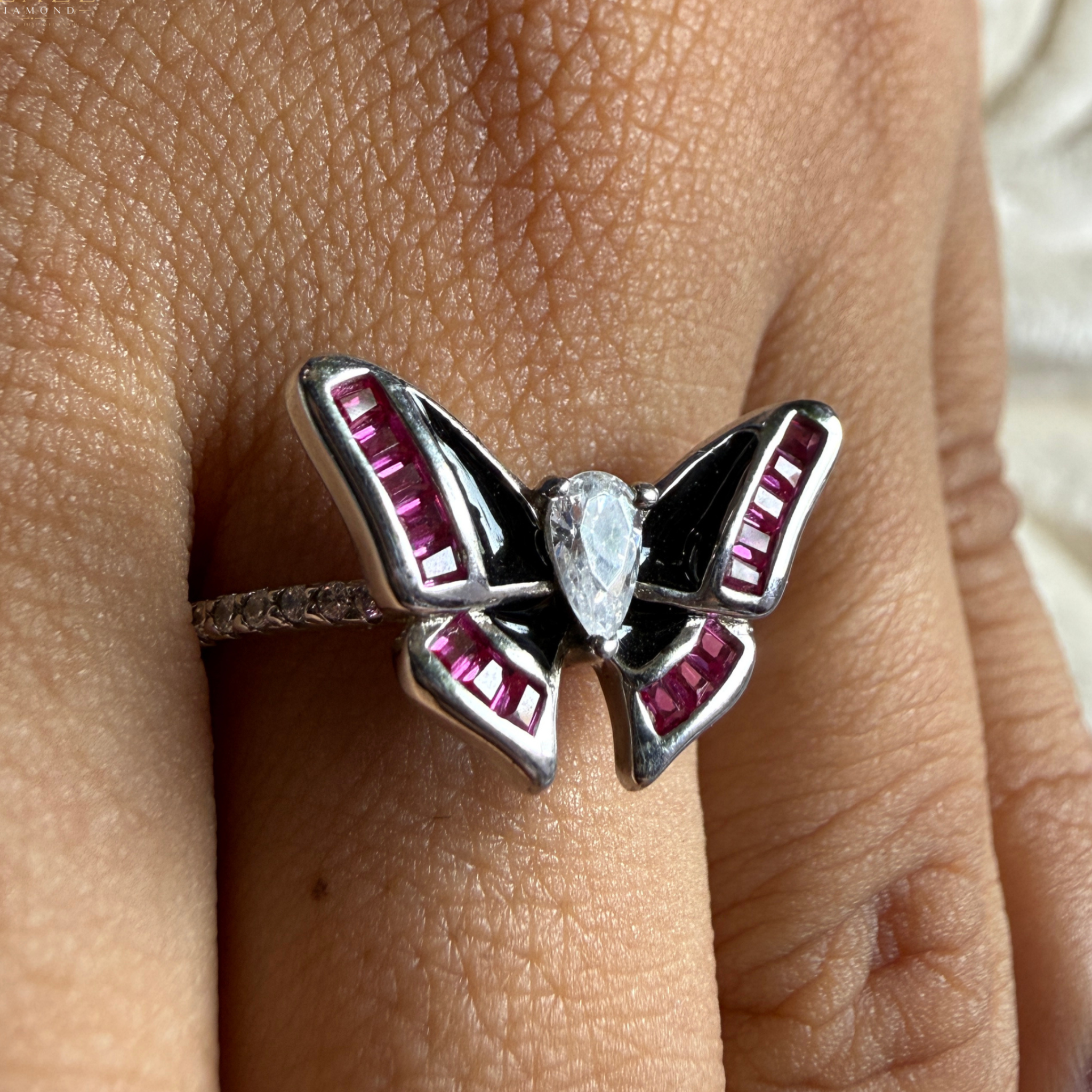 A silver butterfly ring with black enamel and pink gemstone accents, worn on a finger.