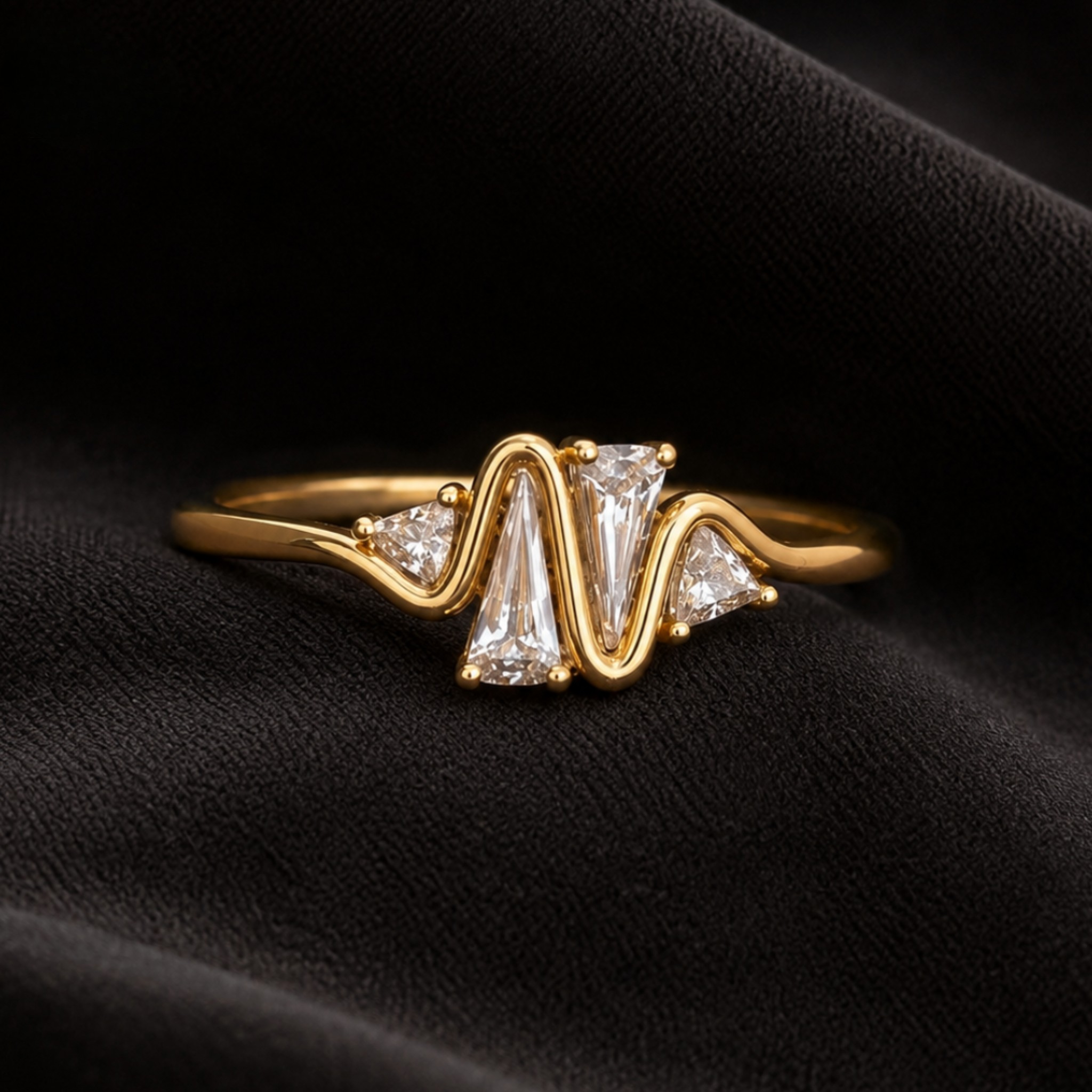 A gold ring with a wavy, zigzag band featuring a central clear baguette diamond flanked by two smaller round diamonds, displayed on a textured black fabric background.