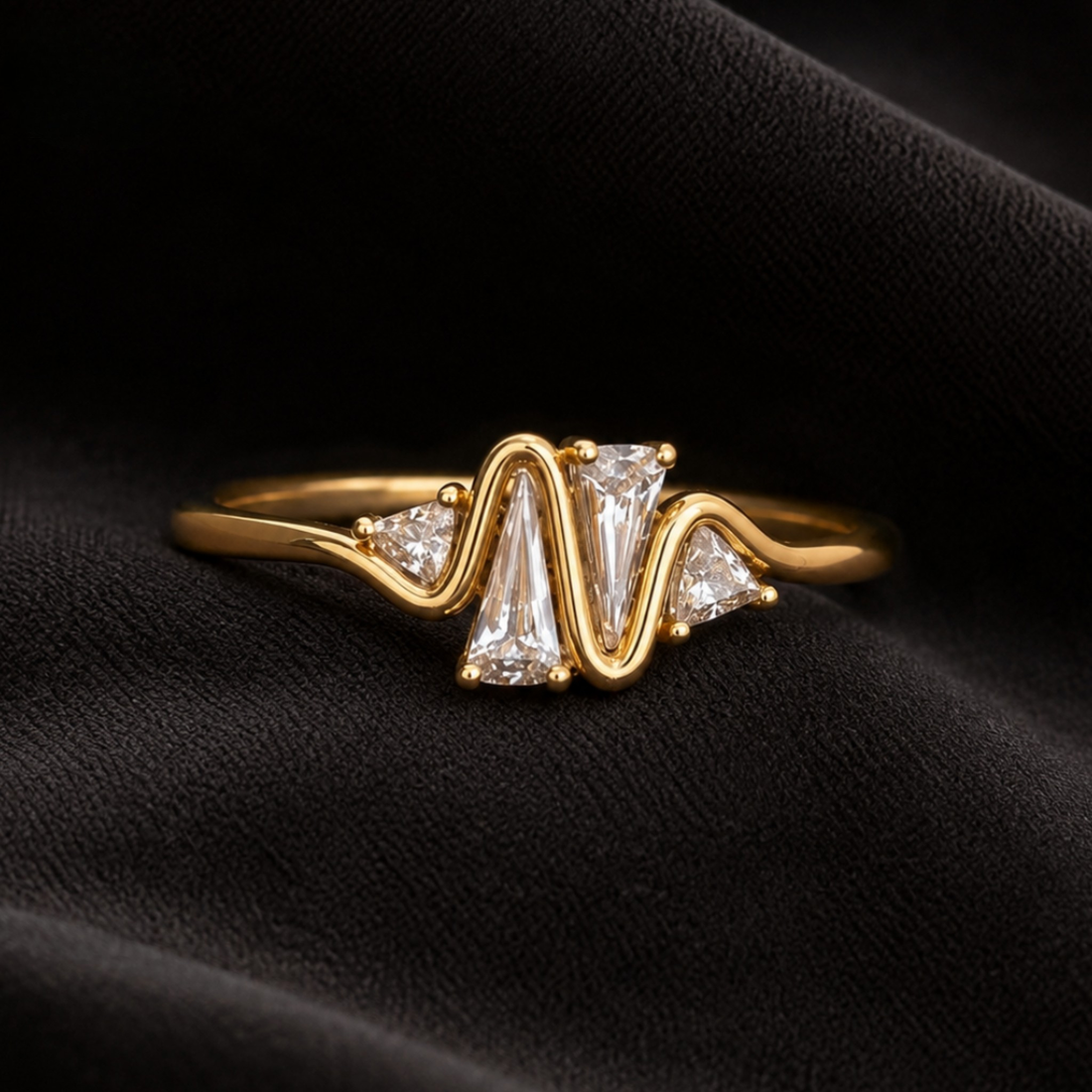 A gold ring with a wavy, zigzag band featuring a central clear baguette diamond flanked by two smaller round diamonds, displayed on a textured black fabric background.