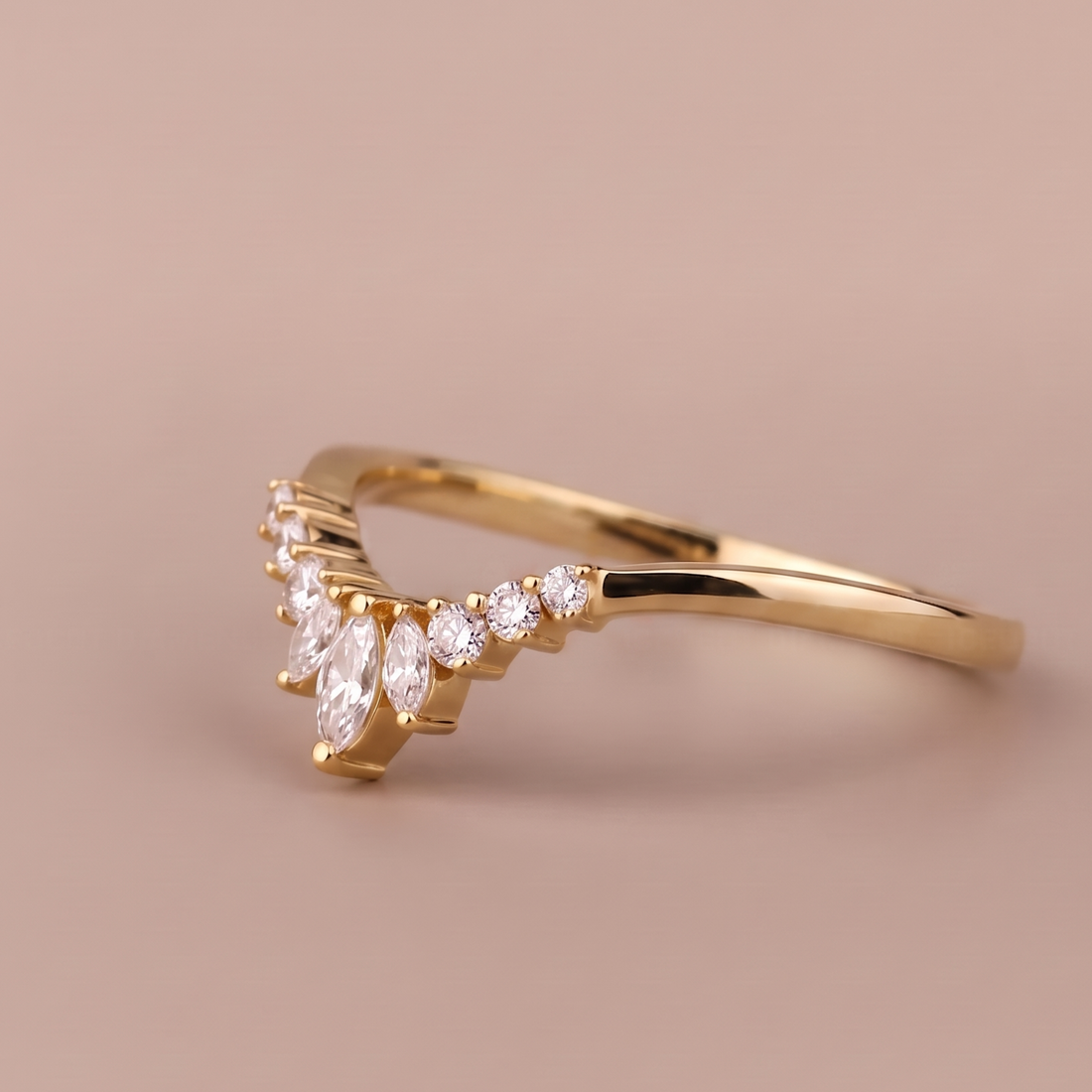 A gold ring with a curved, wave-like top featuring marquise and round clear gemstones, set against a solid warm beige background.