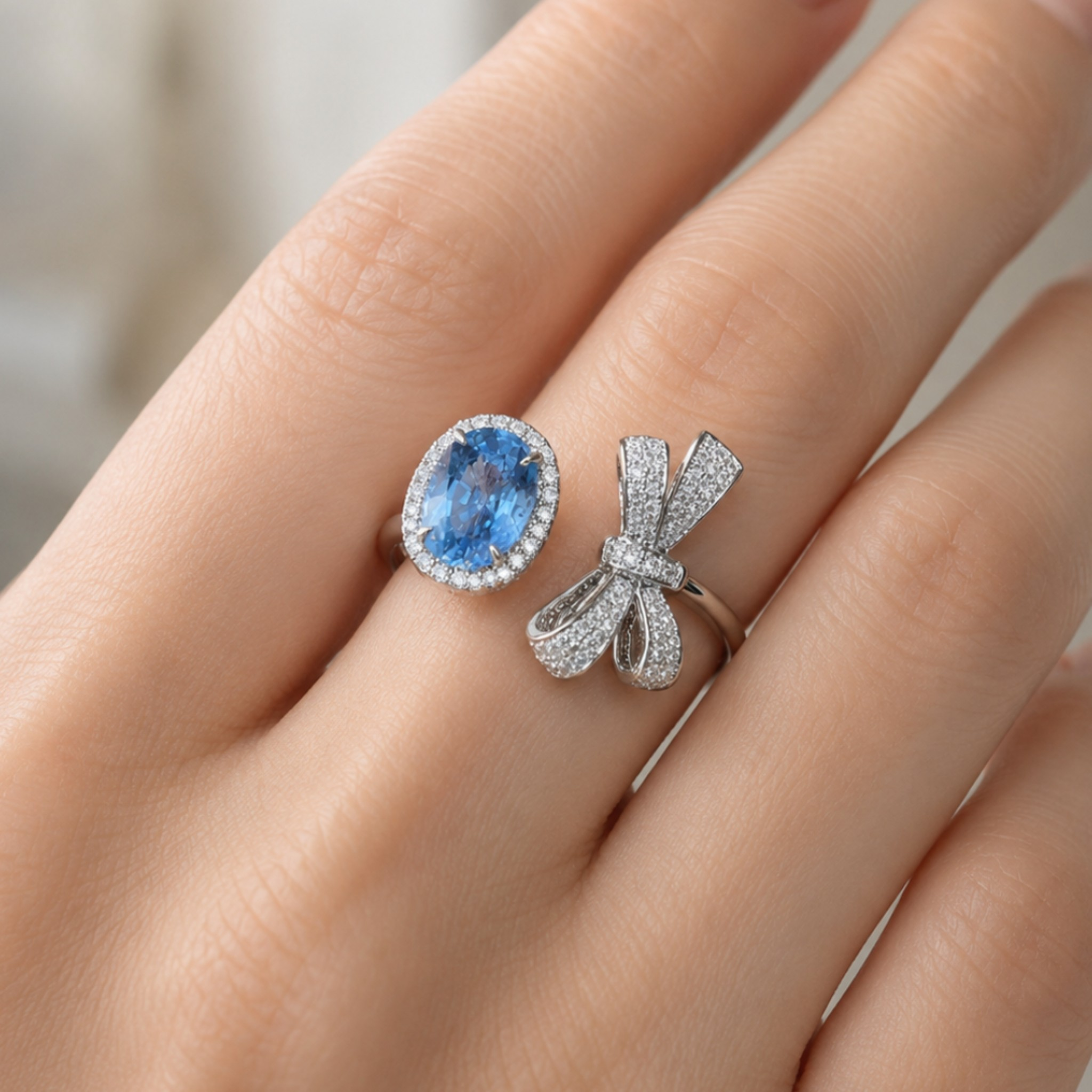 Two silver rings worn on a hand: one with an oval blue gemstone surrounded by small clear stones, and the other a silver bow-shaped ring set with pavé stones.