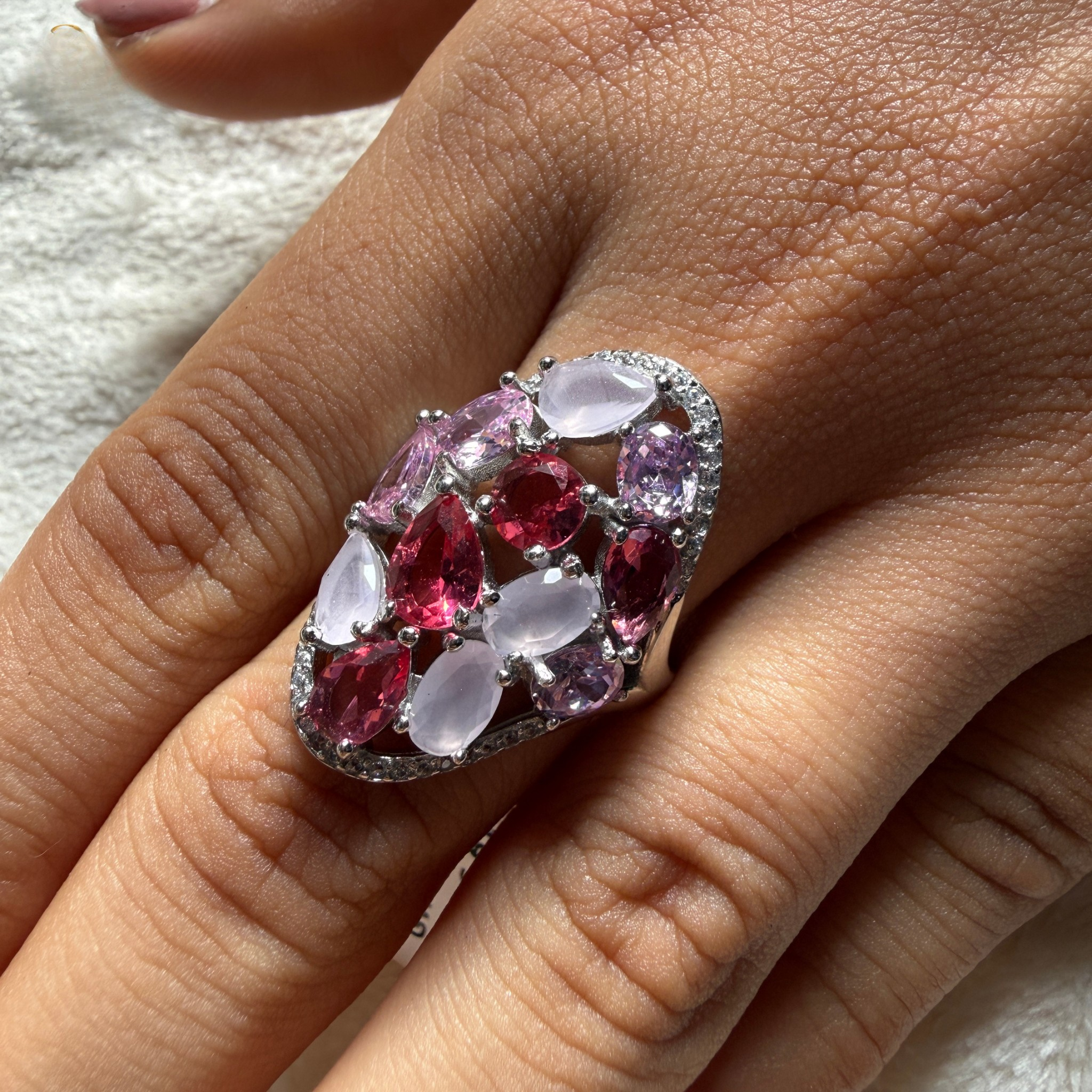 A close-up of a hand wearing a large cluster ring with oval and marquise-cut pink and pale pink stones set in a silver-toned metal.
