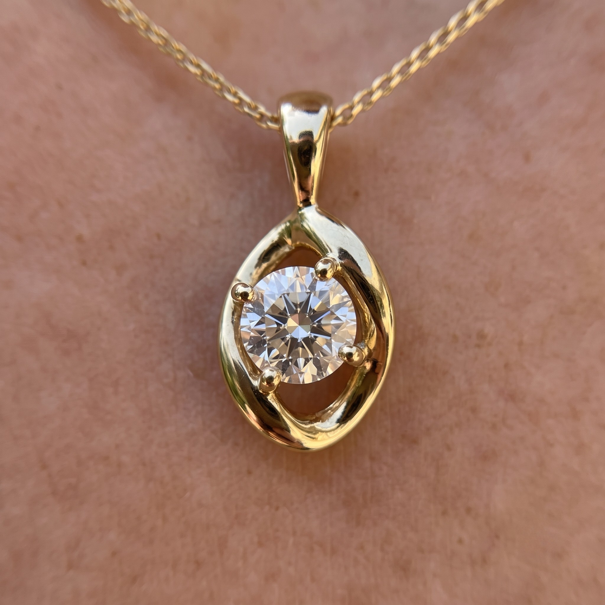 A gold pendant necklace with a round clear gemstone, worn on a person's neck against a light skin tone background.