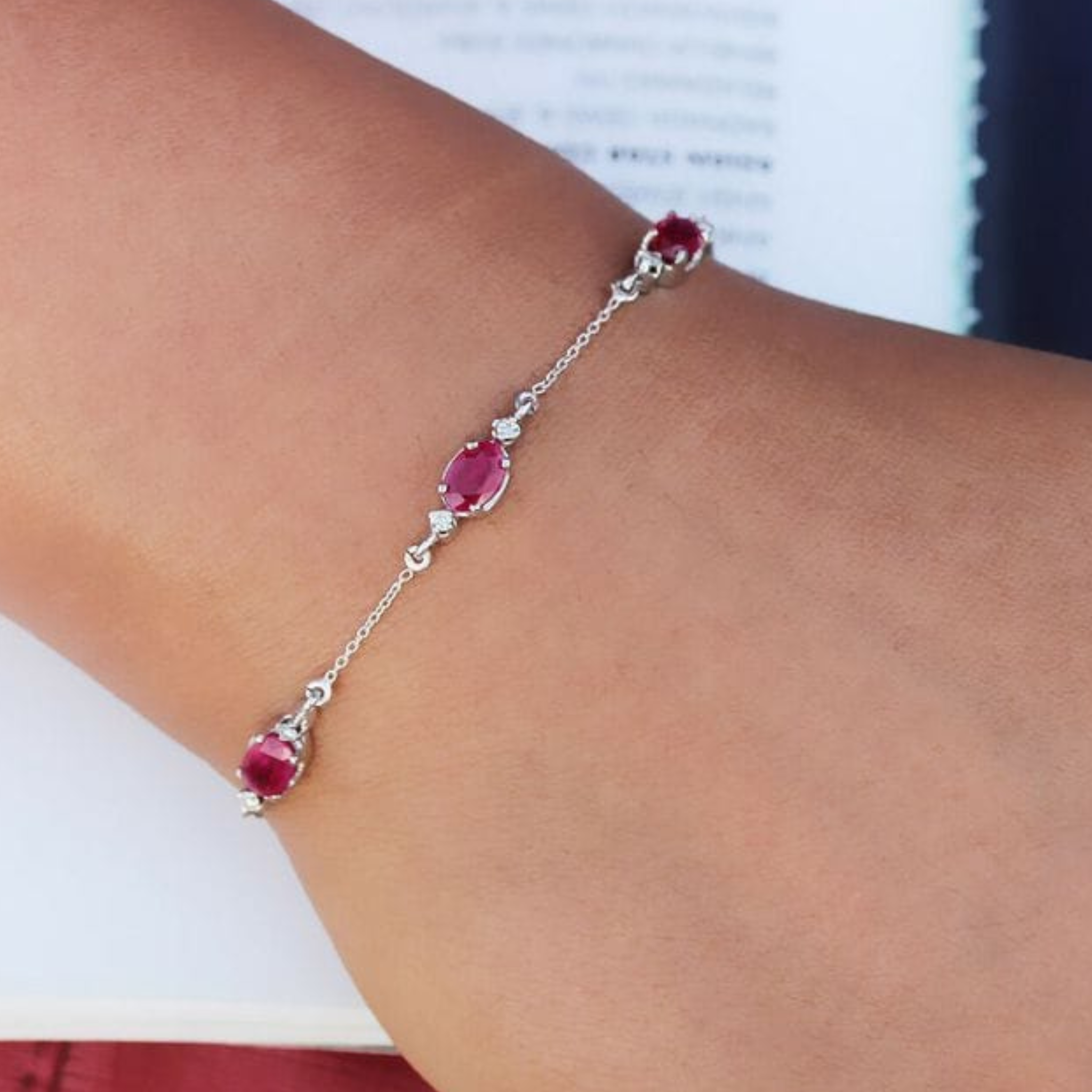 A delicate silver chain bracelet with three oval-cut pinkish-red gemstones, shown worn on a person's wrist.
