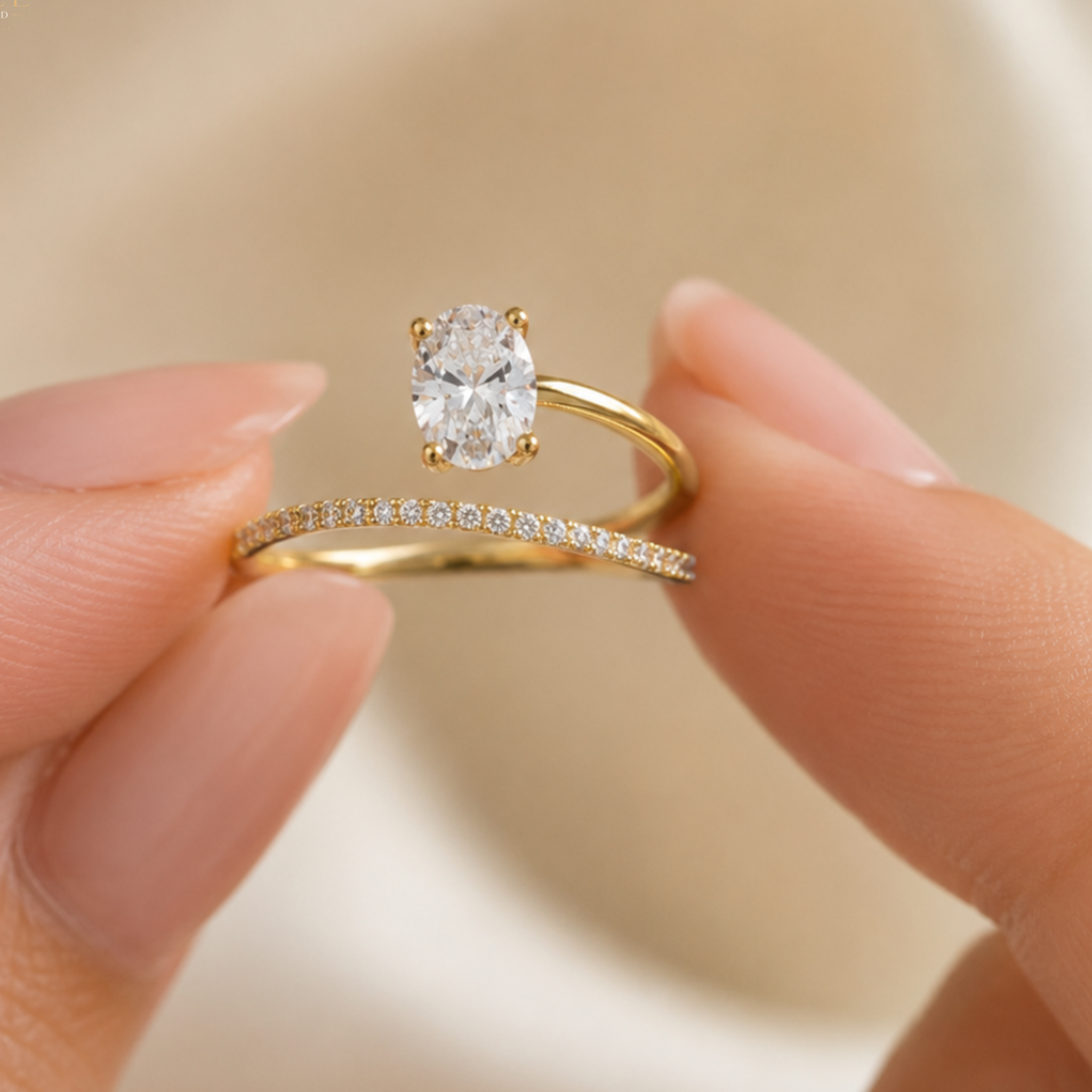 A close-up of a hand holding a yellow gold solitaire engagement ring and a matching gold band with a row of small pavé-set diamonds against a soft beige background.