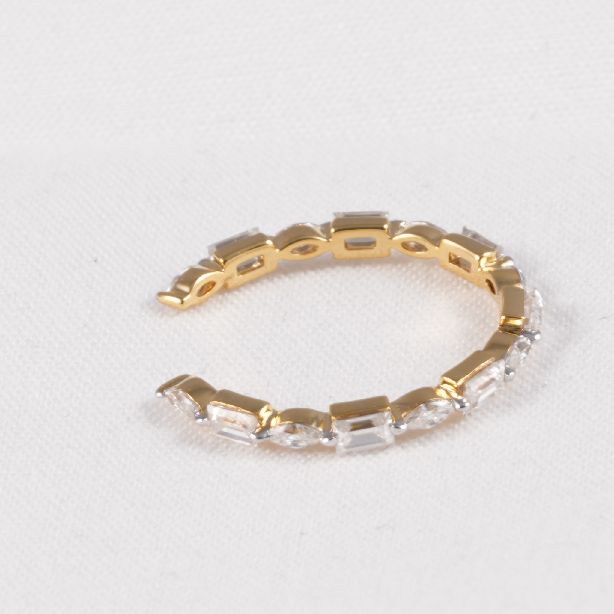 A gold-plated stretch bracelet featuring a row of clear rectangular baguette crystals, displayed on a textured white background.