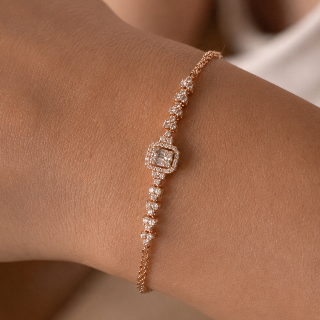 A delicate rose gold bracelet with clear pavé-set stones, featuring a central square halo and dangling stone sections, shown worn on a wrist.