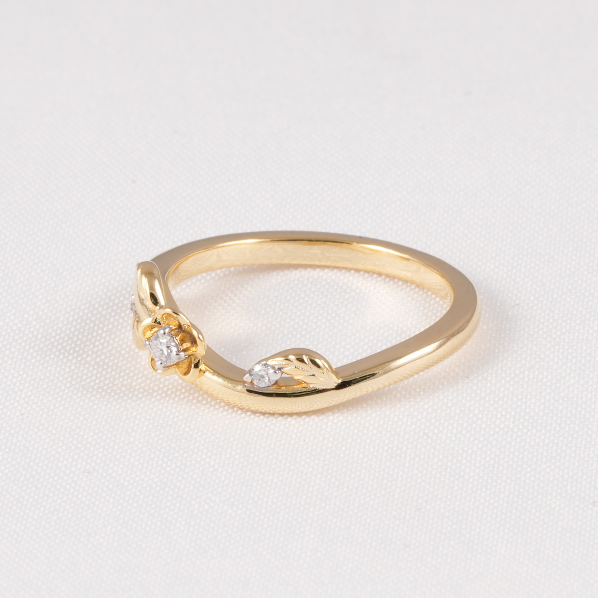 A gold ring featuring a small central clear gemstone and leaf-shaped details on either side, photographed on a textured white background.