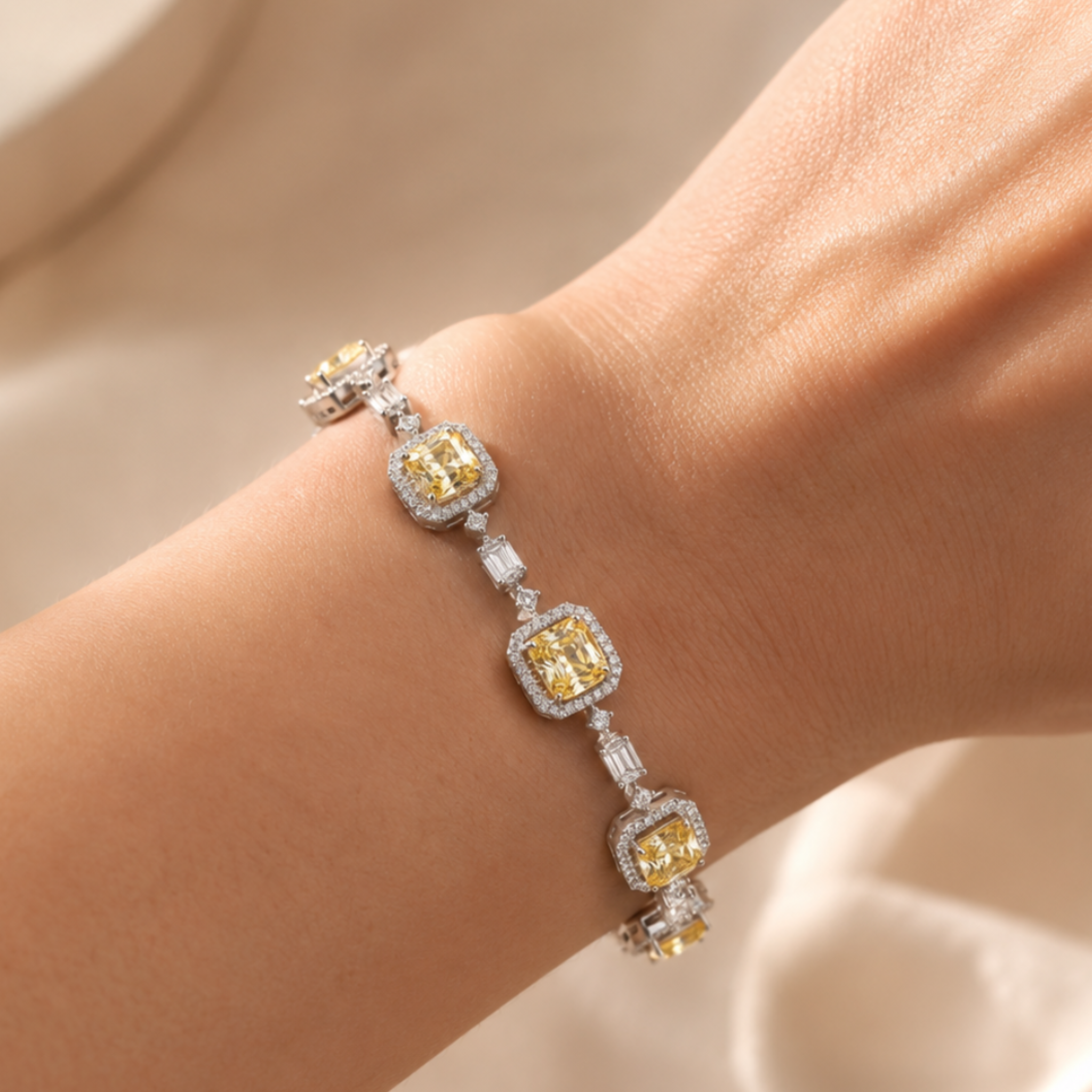 A close-up of a delicate bracelet worn on a wrist. The bracelet features four rectangular yellow gemstone clusters surrounded by silver-toned and white stones, connected by small silver links.