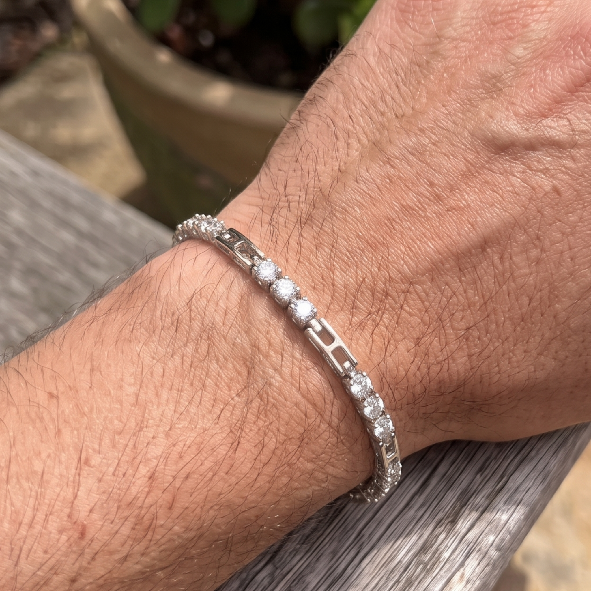 A close-up of a person's wrist wearing a silver tennis bracelet with clear round-cut stones, resting on a weathered wooden surface.