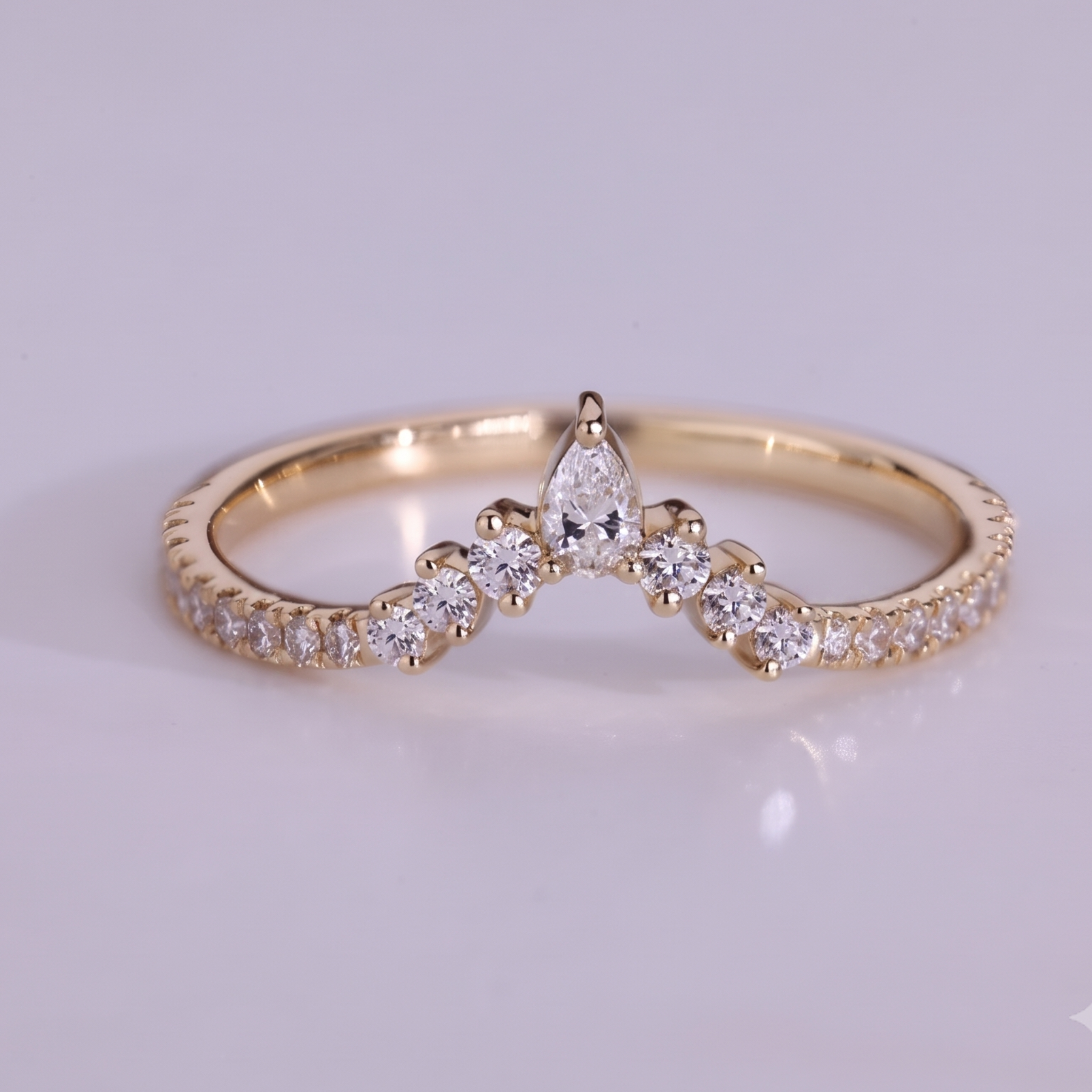 A gold ring with a central pear-cut diamond and smaller marquise and round diamonds along the band, photographed on a light gray background.