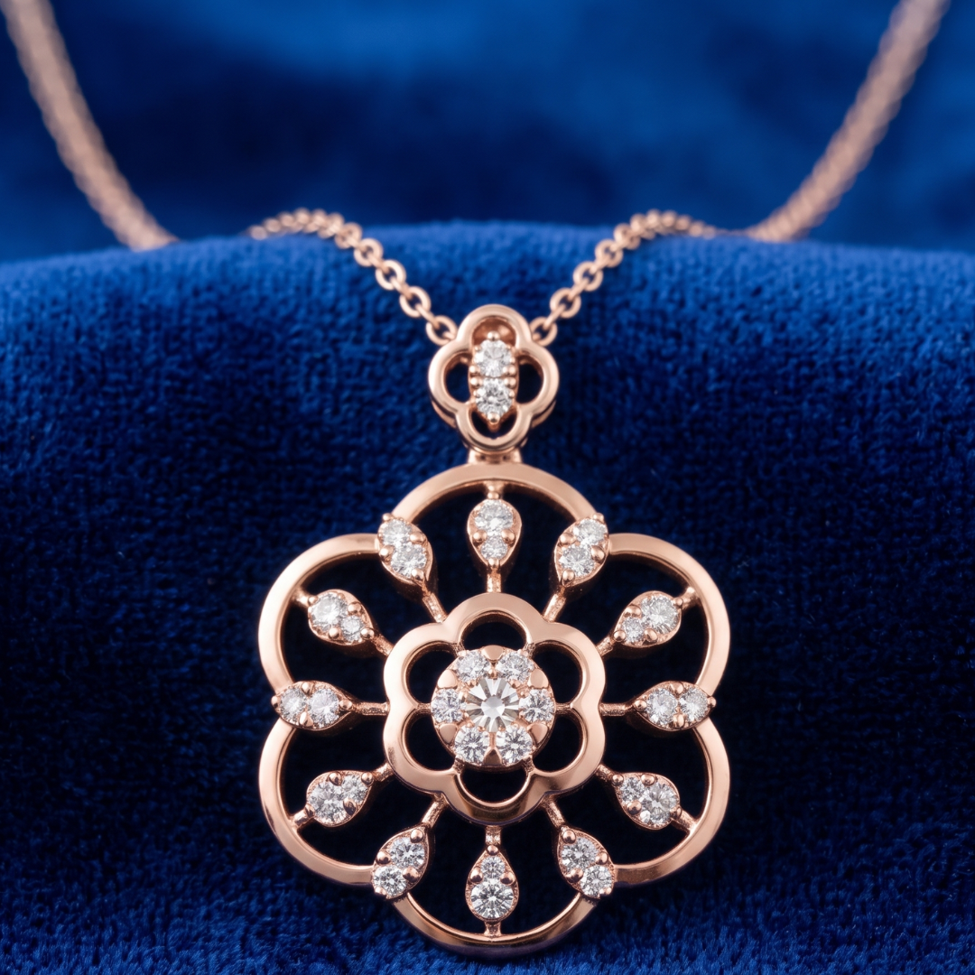 Rose gold floral pendant necklace with clear gemstones, displayed on a textured blue velvet surface.