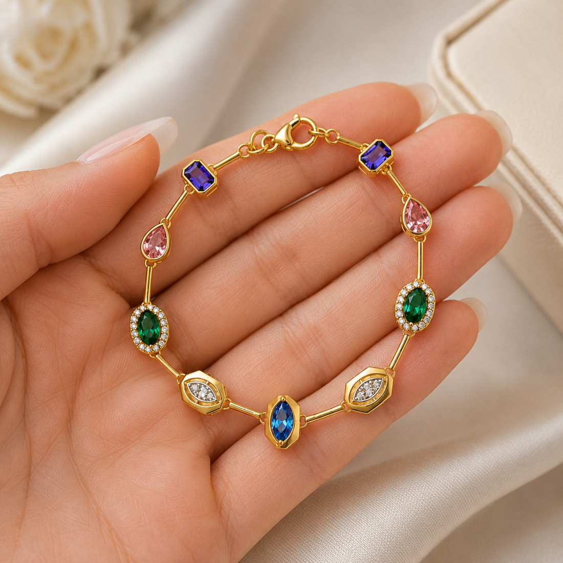 A gold-plated bracelet with multiple colorful gemstones, including blue, green, pink, and purple, displayed on a person's hand against a soft beige background.