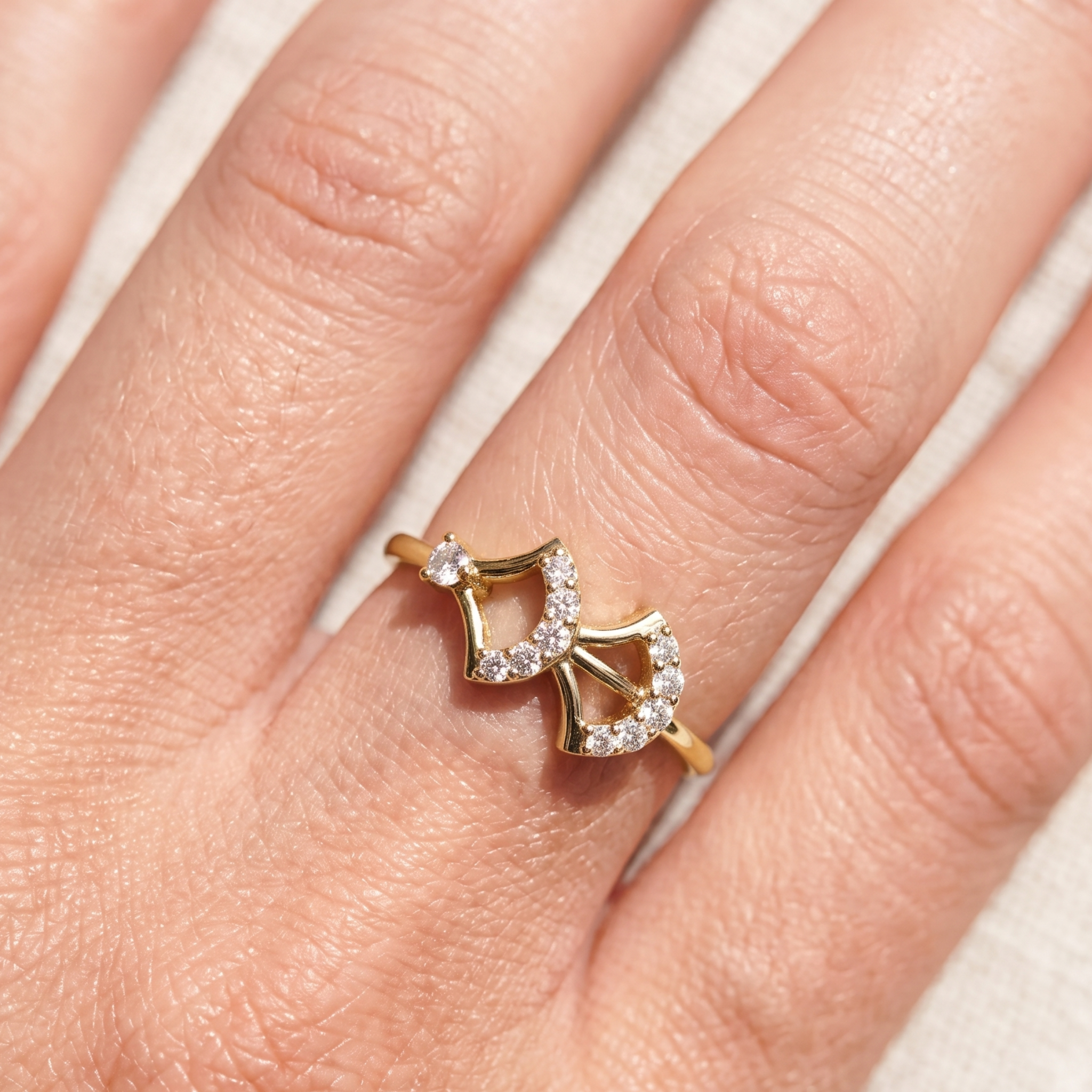 A gold ring with a bow-shaped design set with small clear gemstones, shown worn on a finger.