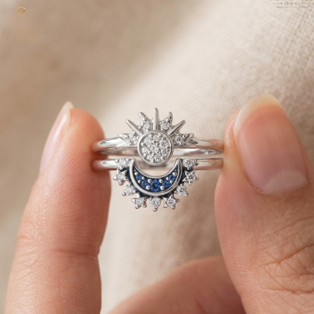A close-up of a hand holding a silver-toned double ring set featuring a sunburst and crescent moon design with clear stones and a blue crescent inlay.