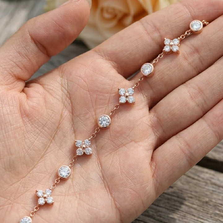 A delicate rose gold chain bracelet with small clear gemstone floral and round bead accents, displayed across an open hand.