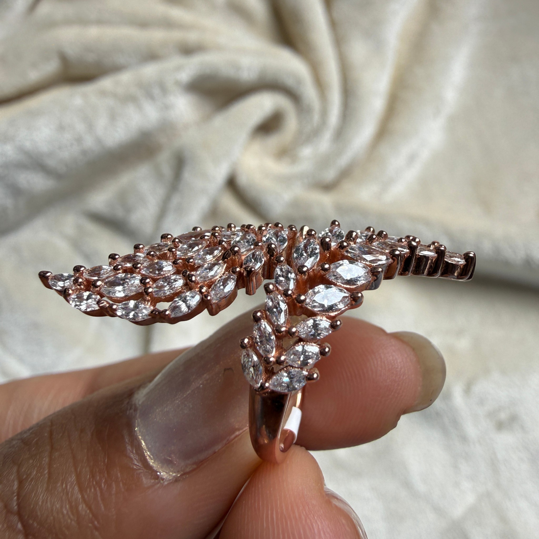 A rose gold butterfly ring with clear marquise-cut gemstones, held between fingers against a soft beige fabric background.