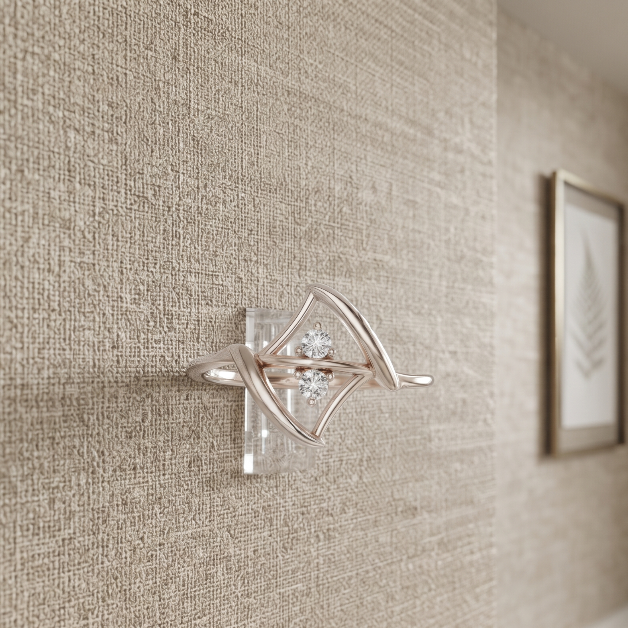 A silver-toned wall-mounted jewelry display stand with a clear acrylic base and a diamond-shaped cradle holding a small cluster of clear stones, shown mounted on a textured beige wall.