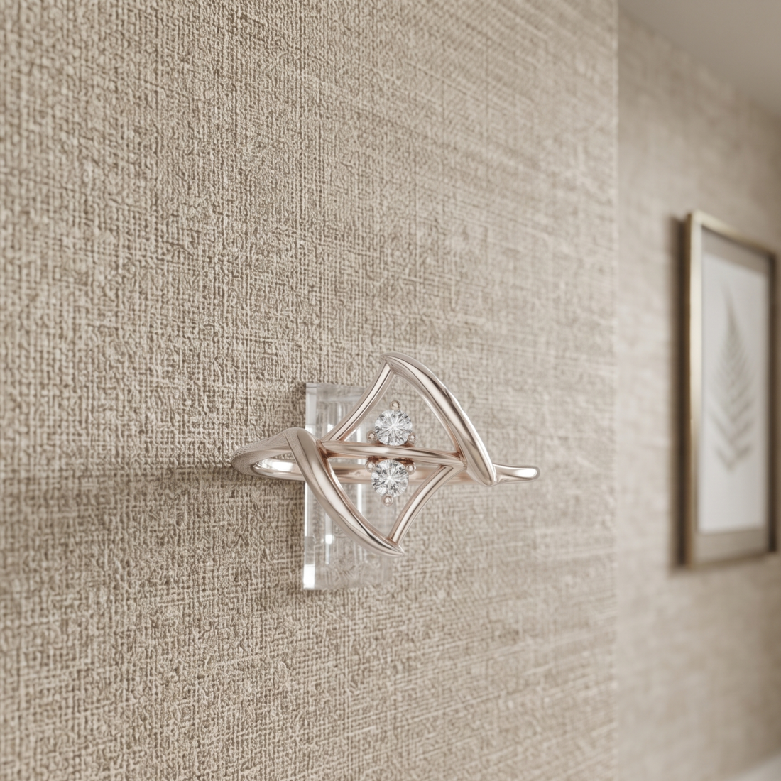 A silver-toned wall-mounted jewelry display stand with a clear acrylic base and a diamond-shaped cradle holding a small cluster of clear stones, shown mounted on a textured beige wall.