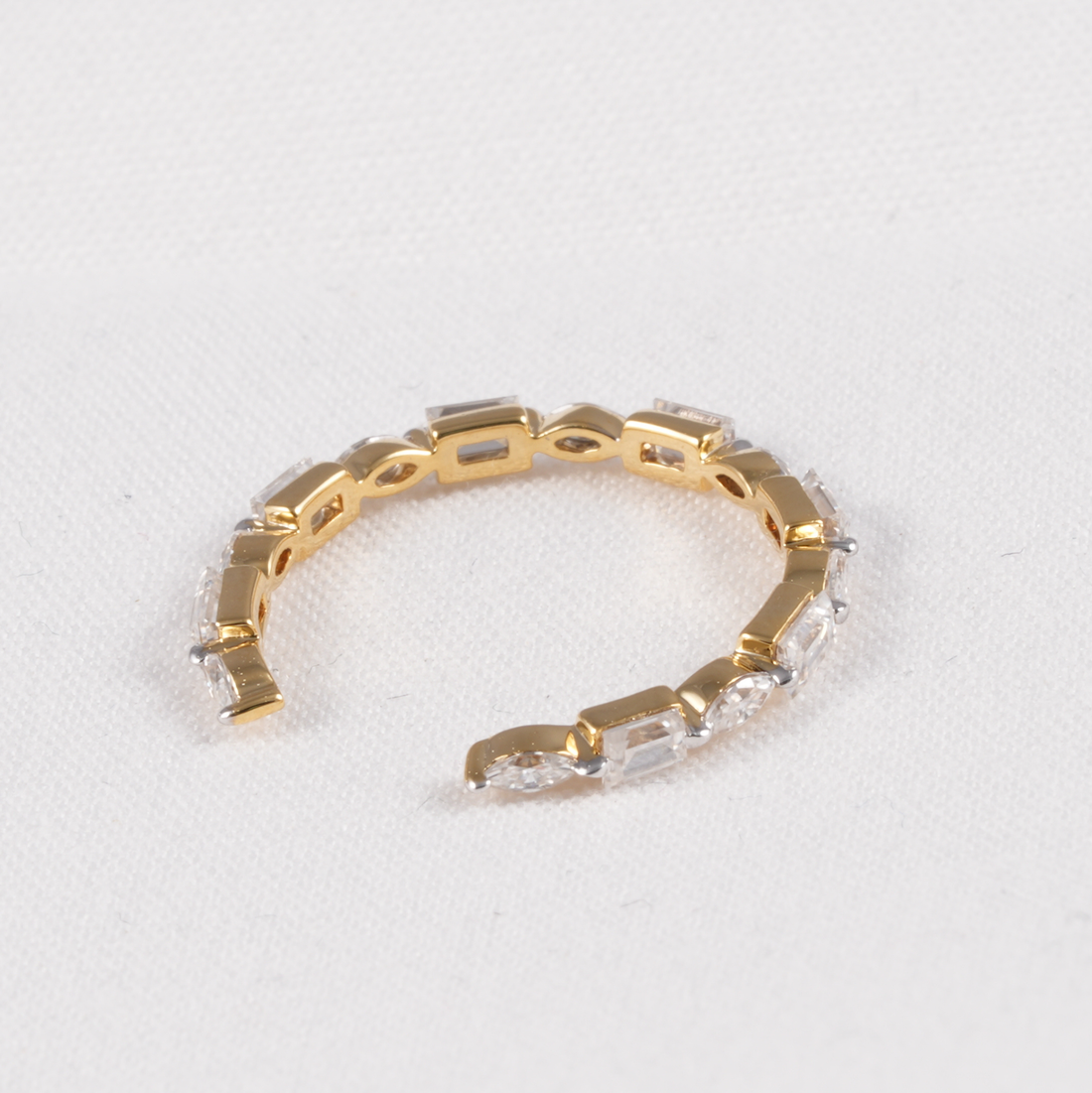A gold tennis bracelet with clear rectangular baguette and round-cut crystals, displayed on a textured white background.