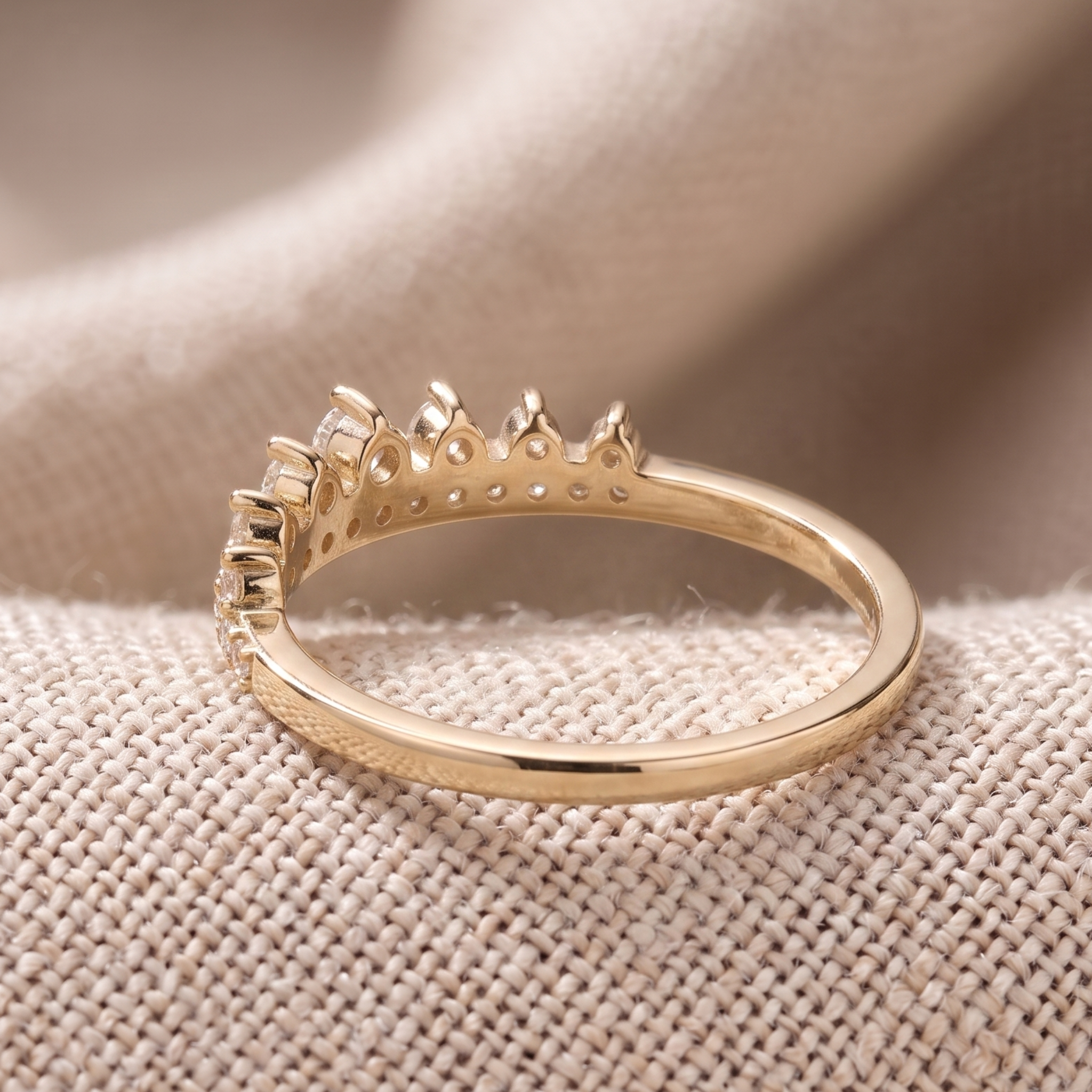 A gold ring with a crown-like top setting, photographed close-up on a textured beige fabric surface.